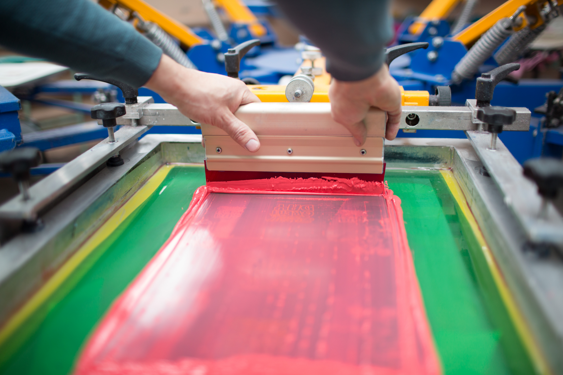 Worker pulling red ink across a screen-printing press in a workshop