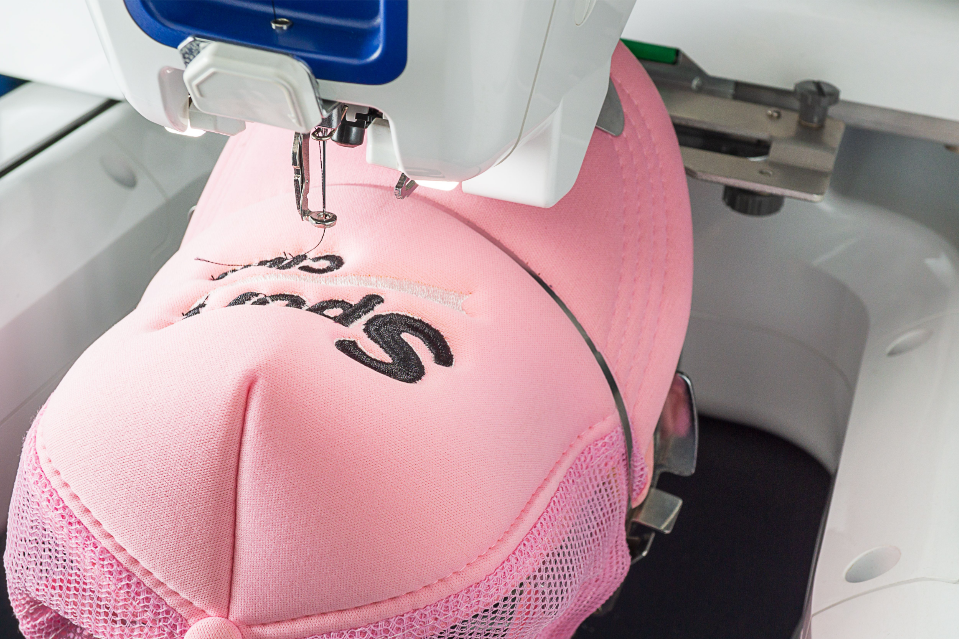 Embroidery machine stitching black text onto a pink cap in close-up.