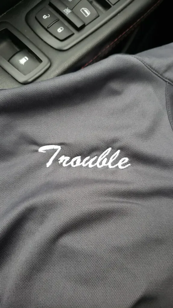 Black fabric with the word “Trouble” embroidered in white beside a car console.