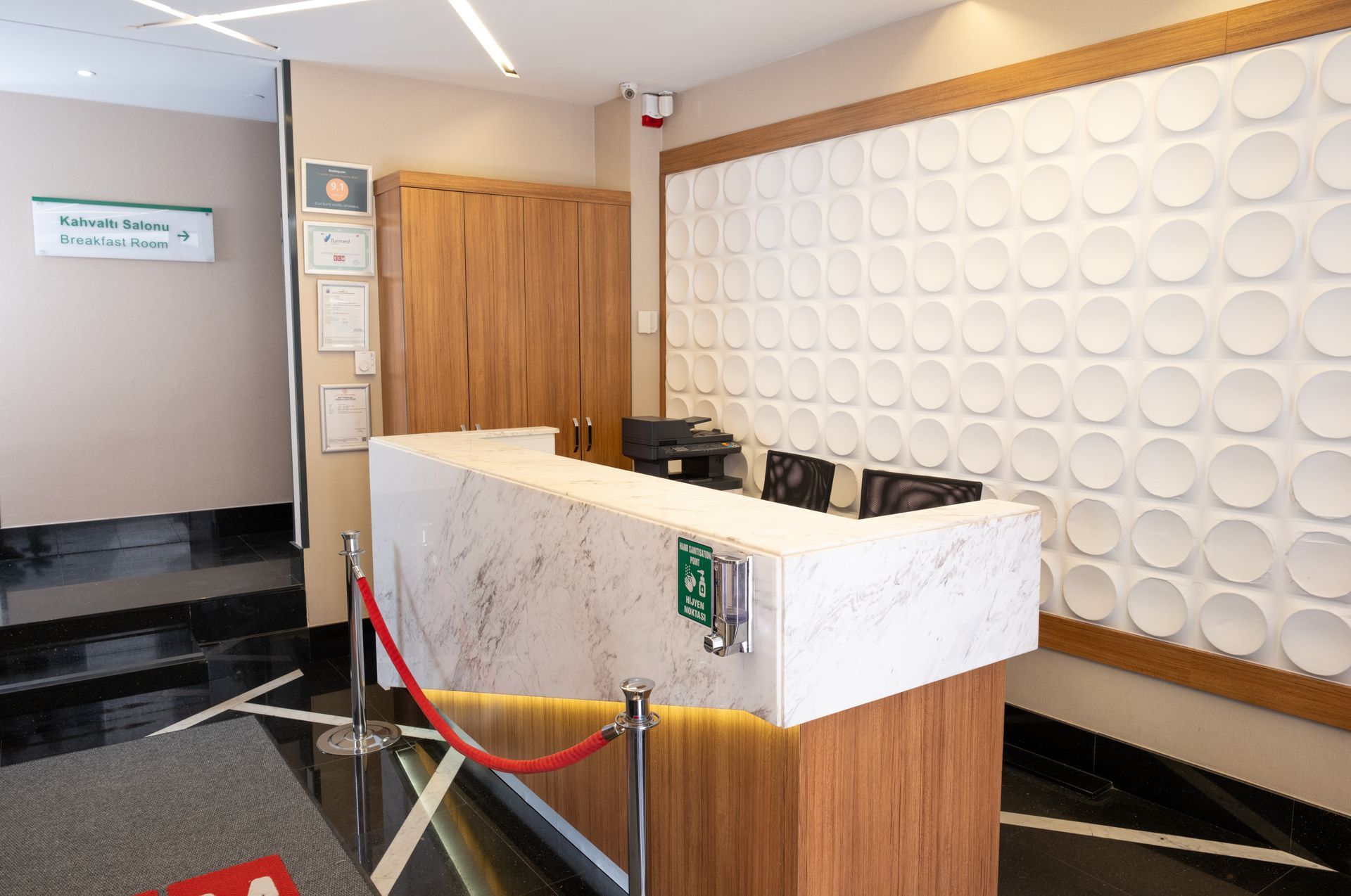 Hotel lobby with a reception desk. A large painting of a coastal city scene hangs on a wall.