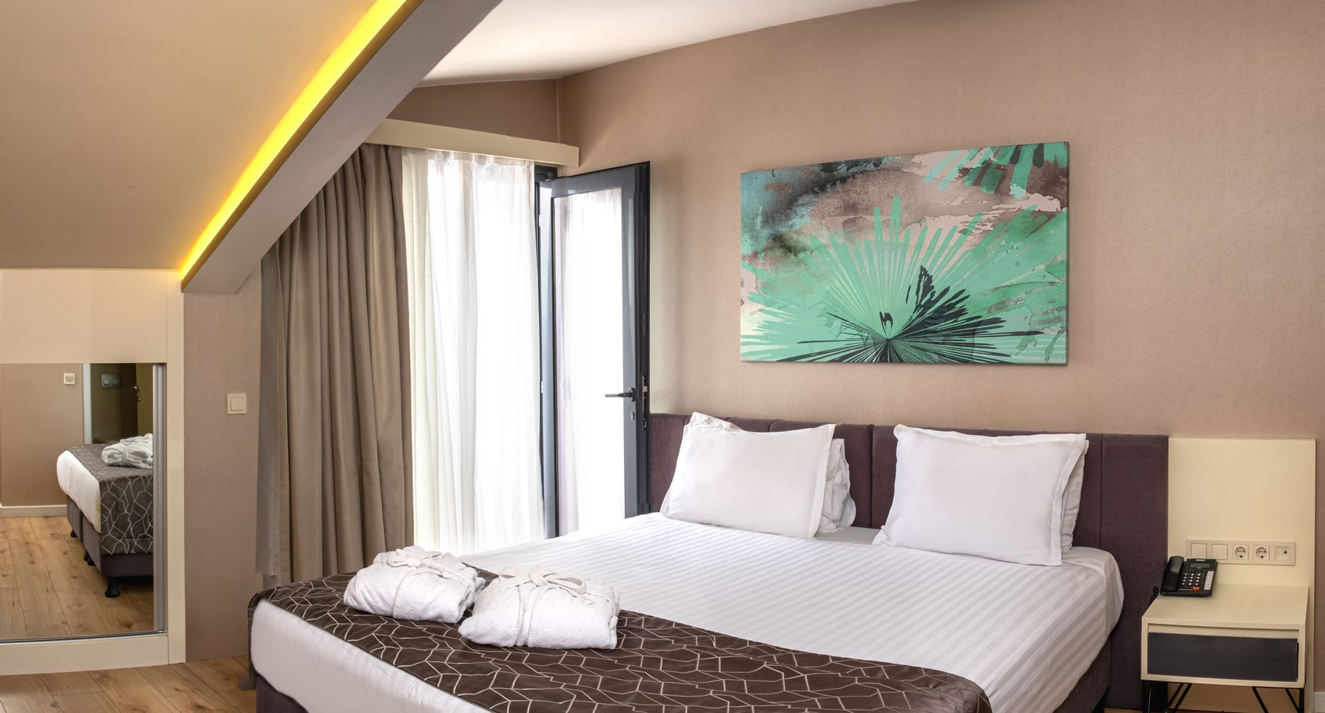 A hotel bedroom with a bed, balcony, and artwork; brown, red, and white decor. Angled ceiling and wooden floor.