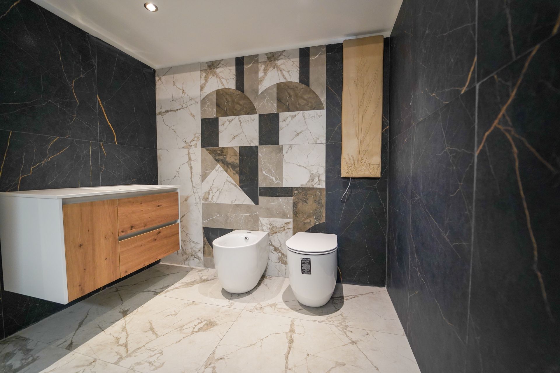 Bagno moderno con pareti in pietra scura, pavimento in marmo chiaro, mobiletto in legno e bidet e WC bianchi a filo con la parete piastrellata.