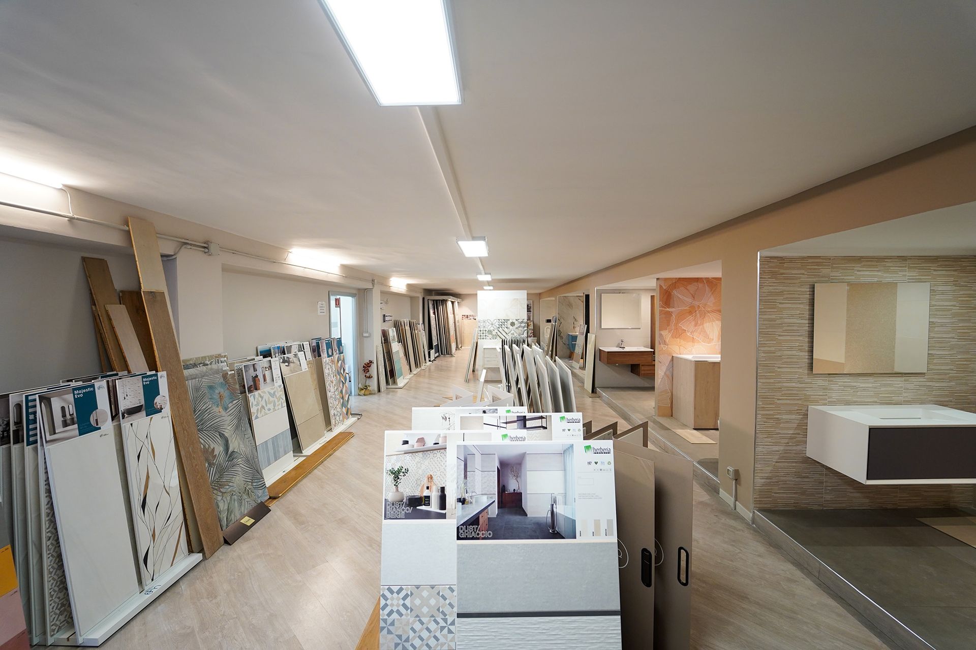Uno showroom con file di campioni di piastrelle, pannelli espositivi e mobili da bagno moderni, il tutto su pareti neutre.