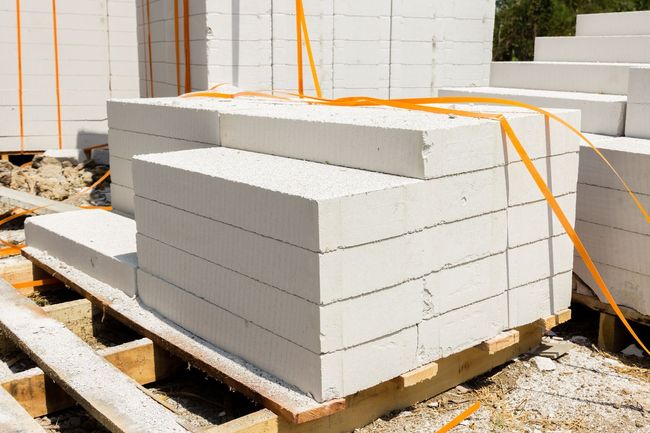 In un cantiere edile, un pallet di blocchi di cemento rettangolari bianchi impilati e fissati con cinghie di plastica arancioni.