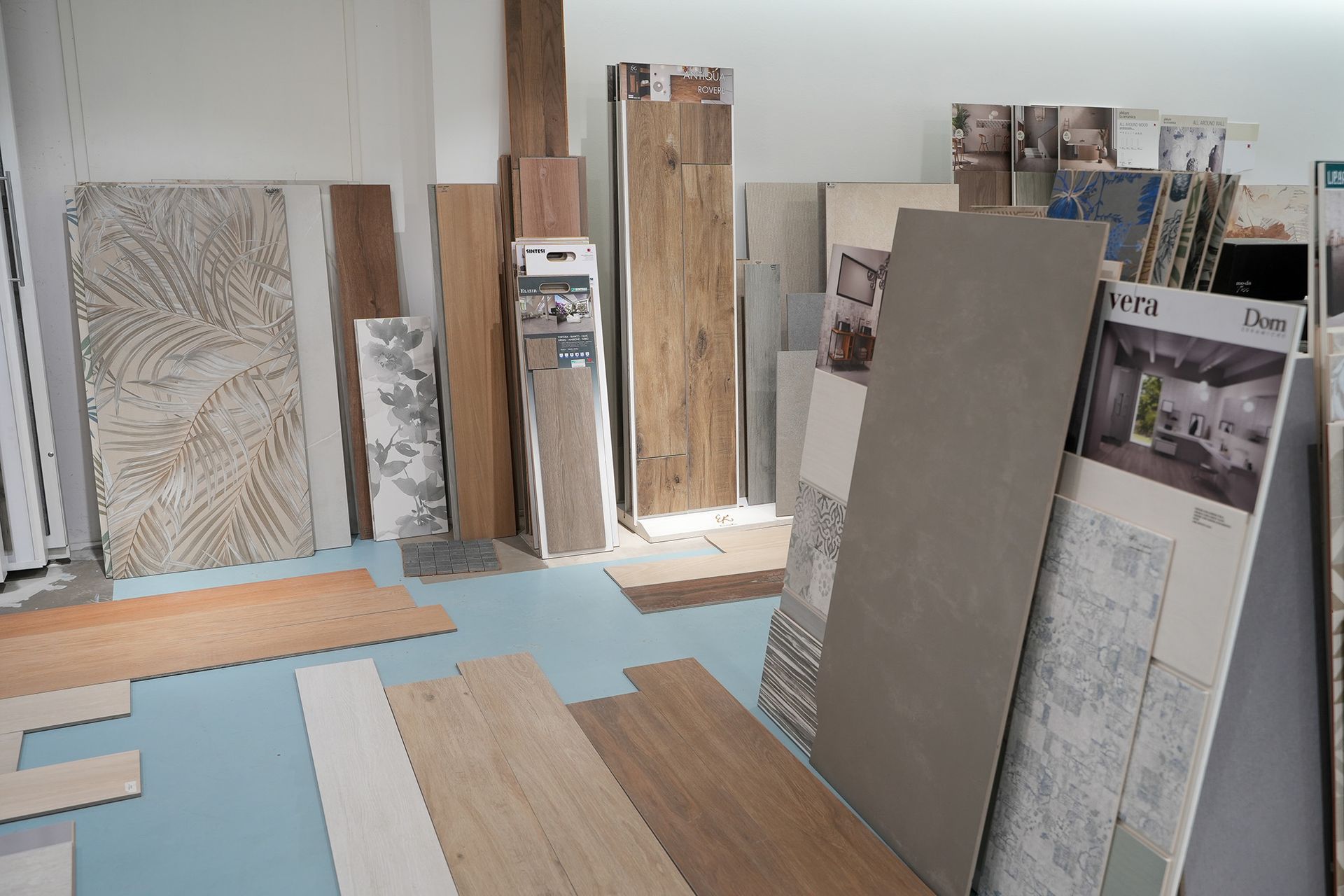 Un'esposizione in showroom che presenta vari campioni di piastrelle e pavimenti effetto legno disposti verticalmente e sul pavimento.