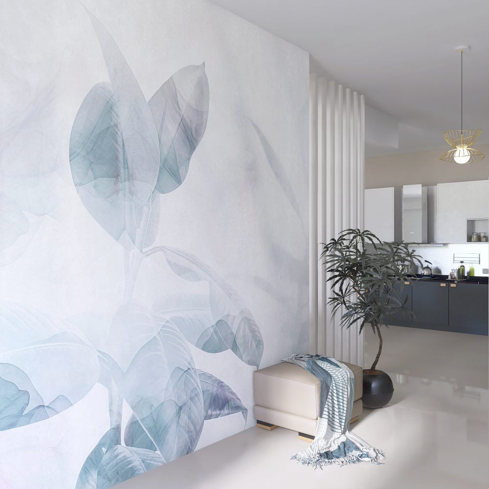 Un murale raffigurante foglie botaniche blu su una parete bianca, accanto a un pouf beige, un plaid decorativo e una pianta in vaso.