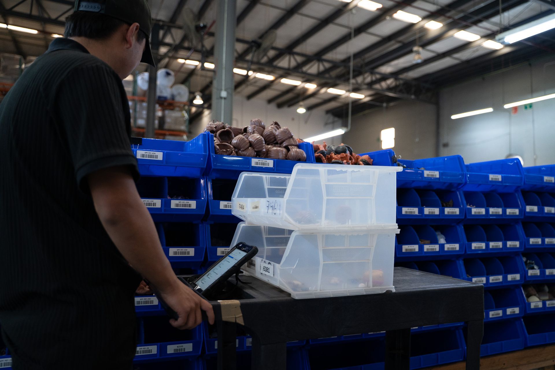 Worker loading white plastic bins onto a cart in a warehouse with blue storage shelves
