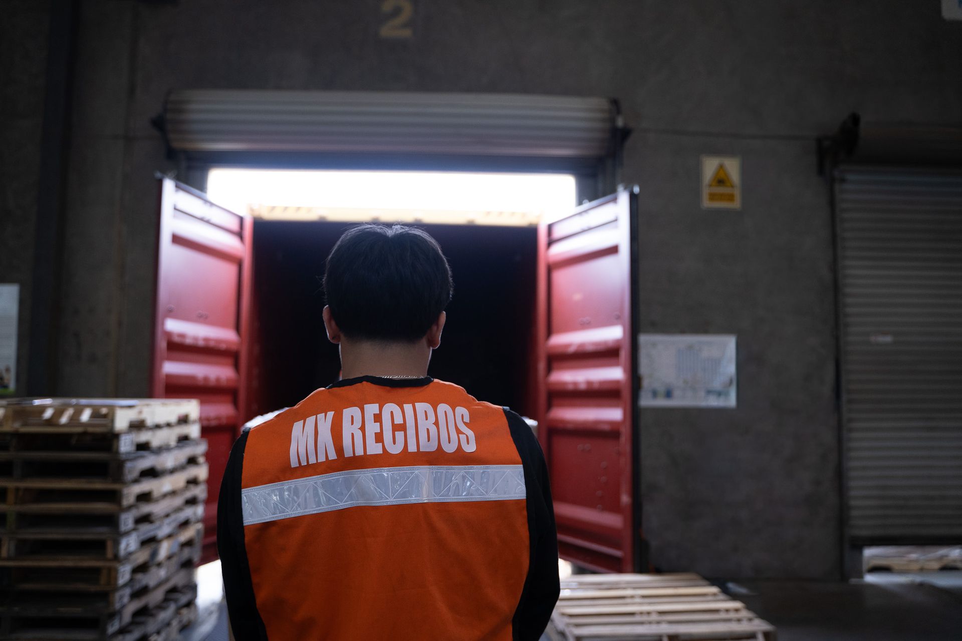 Worker in orange MX Records jacket standing at a loading dock doorway with pallets nearby