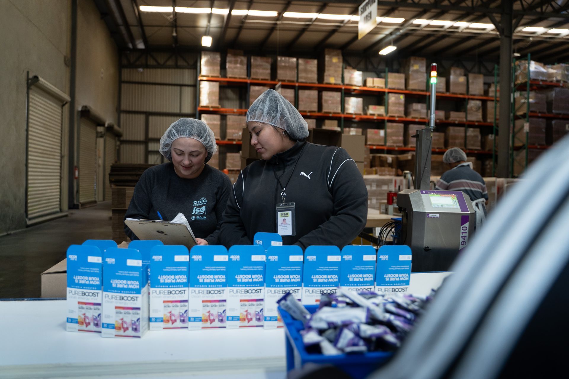 Volunteers packing blue and white food boxes at a warehouse table