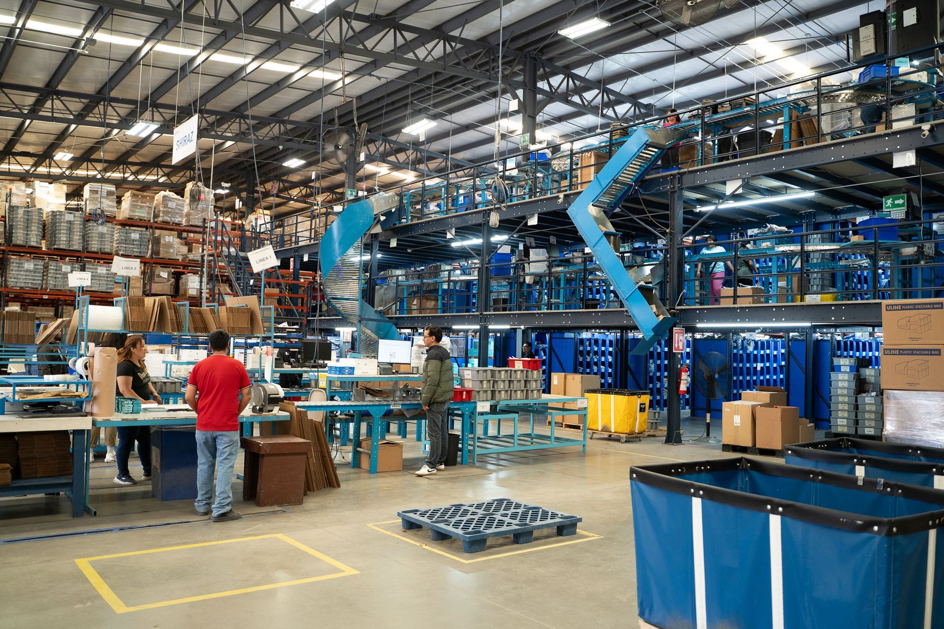 Busy warehouse with workers, conveyor belts, stacked boxes, and blue industrial equipment