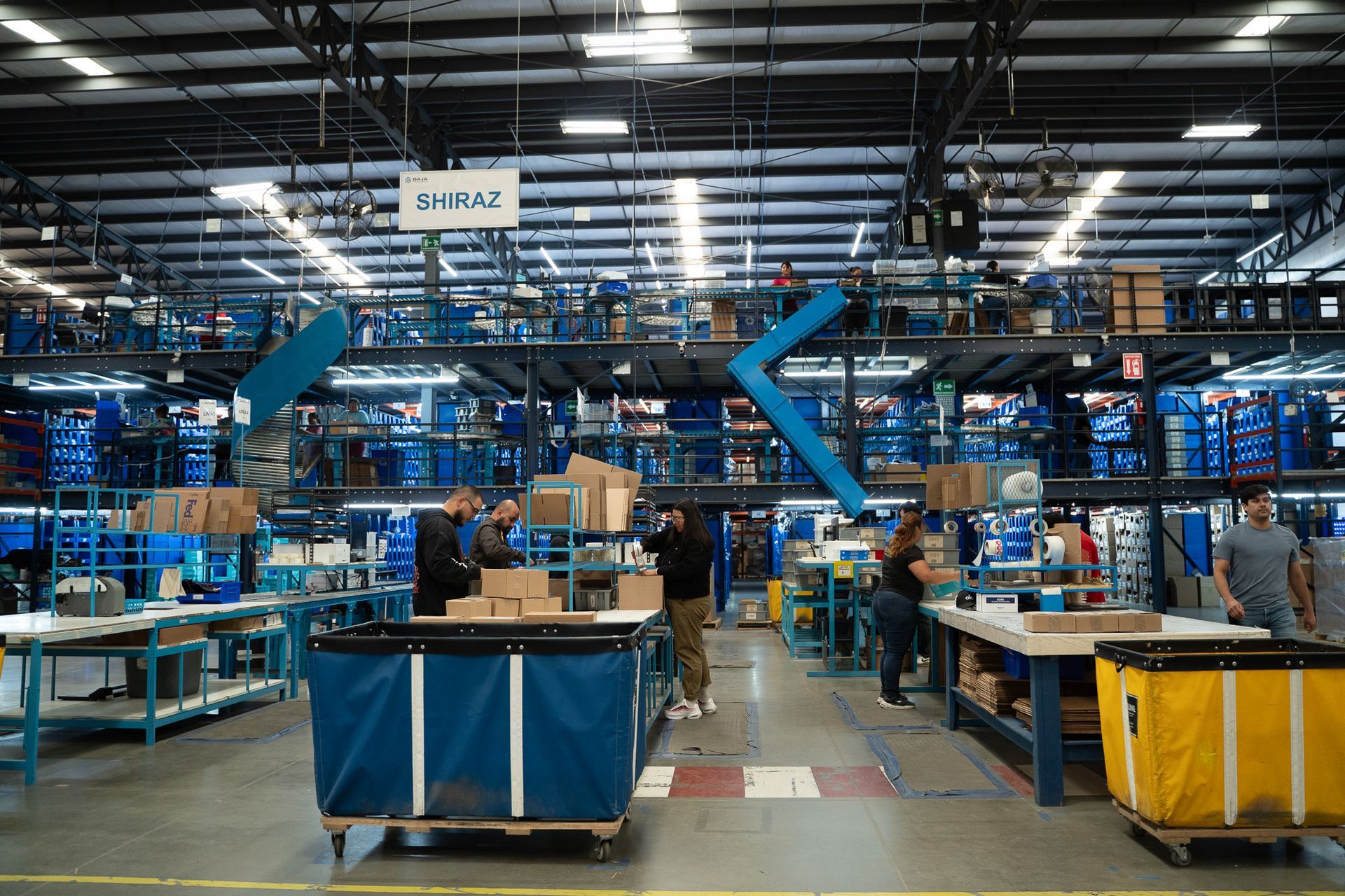 Busy factory assembly line with workers, blue machinery, and carts under bright overhead lights