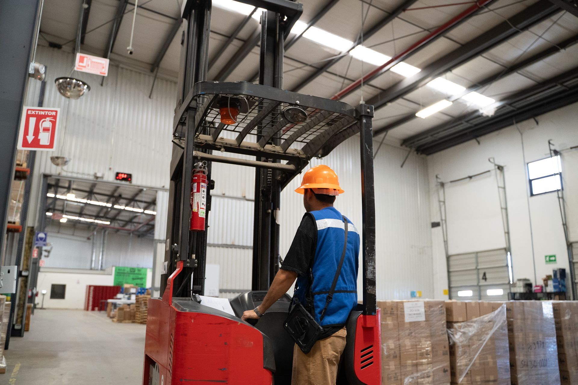 Worker in orange hard hat operating a red forklift inside a warehouse.