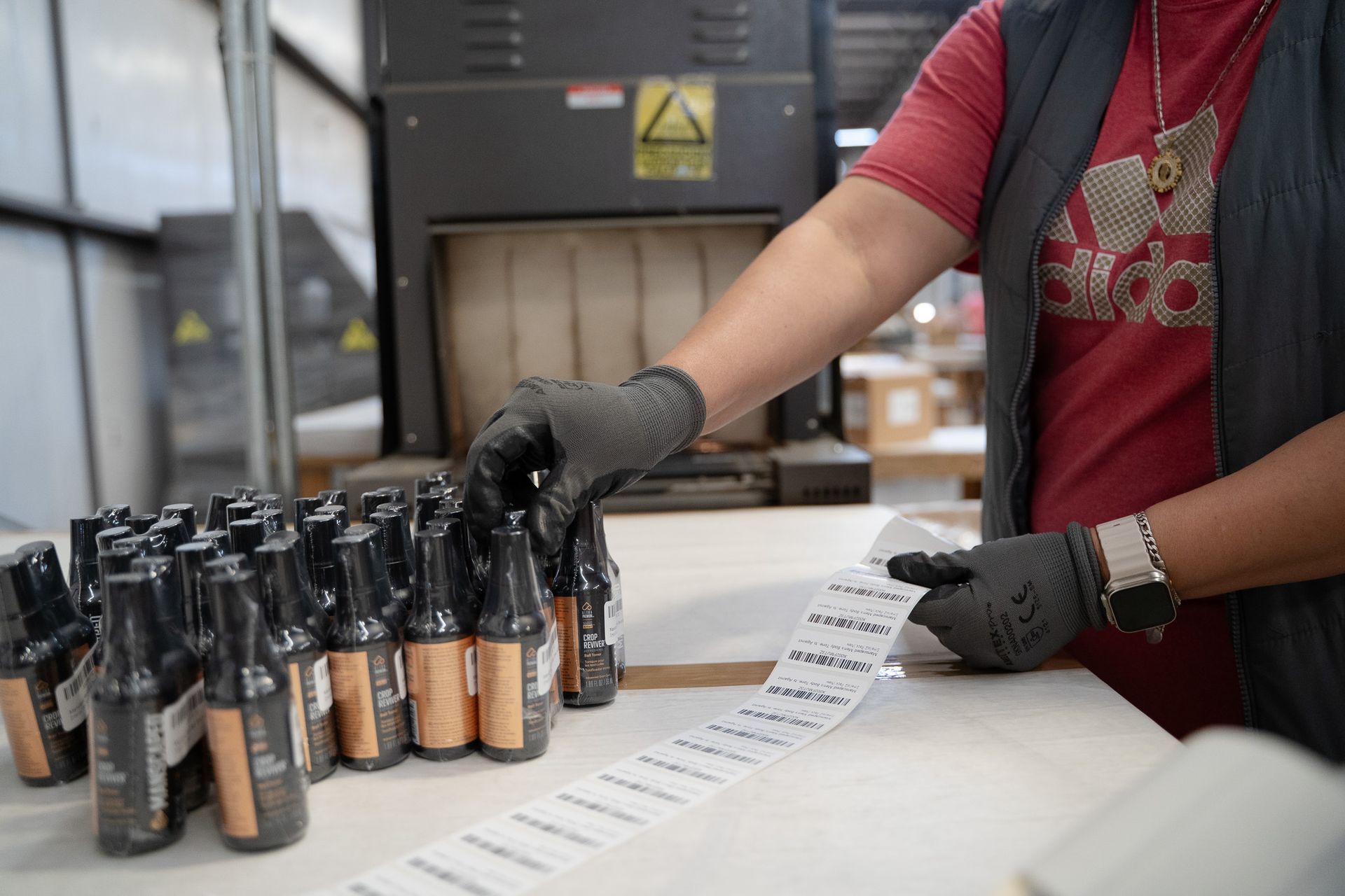 Gloved worker labels rows of bottles beside a machine in an industrial setting
