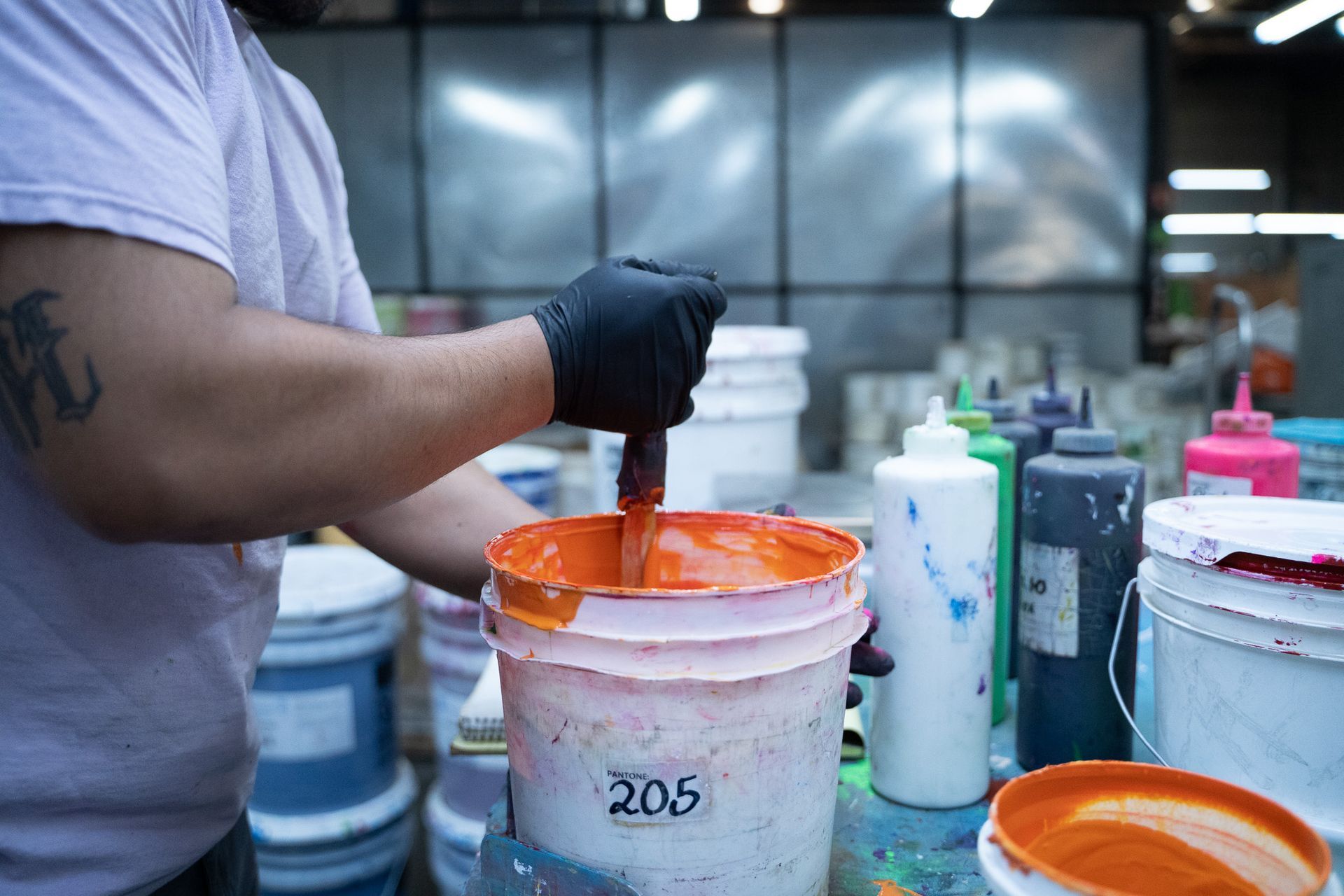 Worker in gloves stirring bright orange paint in a white bucket at a workshop table