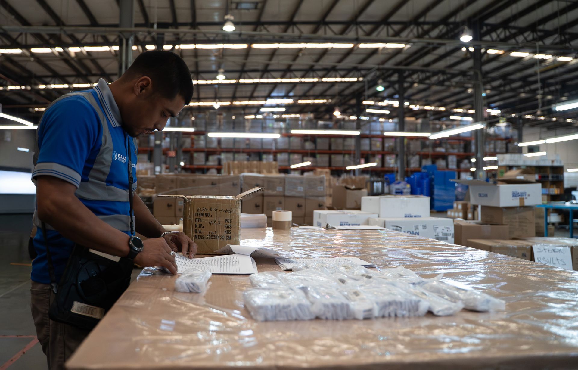 Worker packing items at a warehouse table with wrapped packages and boxes in the background