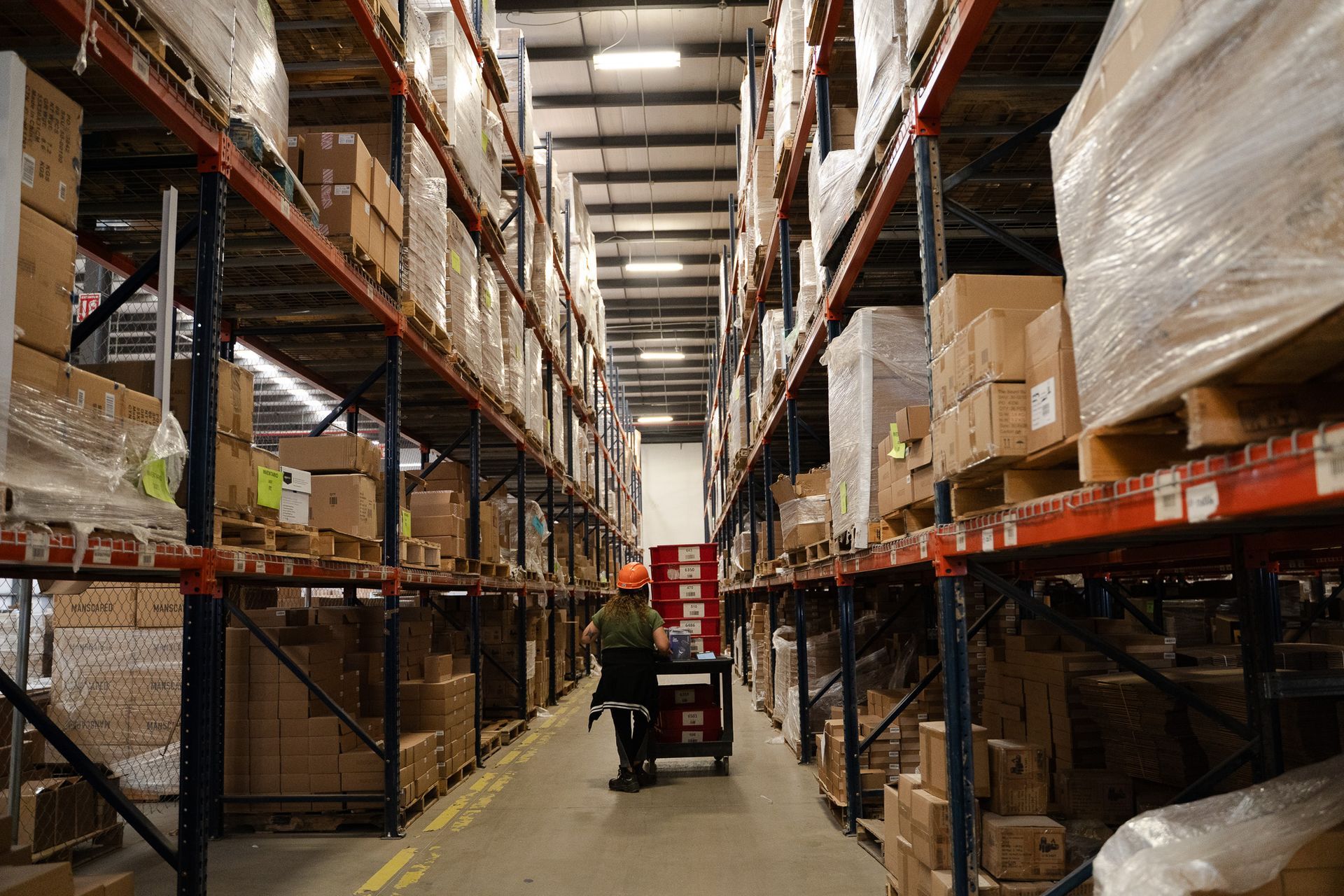 Warehouse aisle with tall racks of boxes and a forklift in the center.