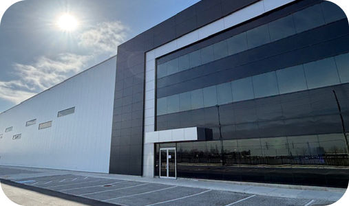 Modern industrial warehouse with white siding, dark glass entrance, and sunlit parking area