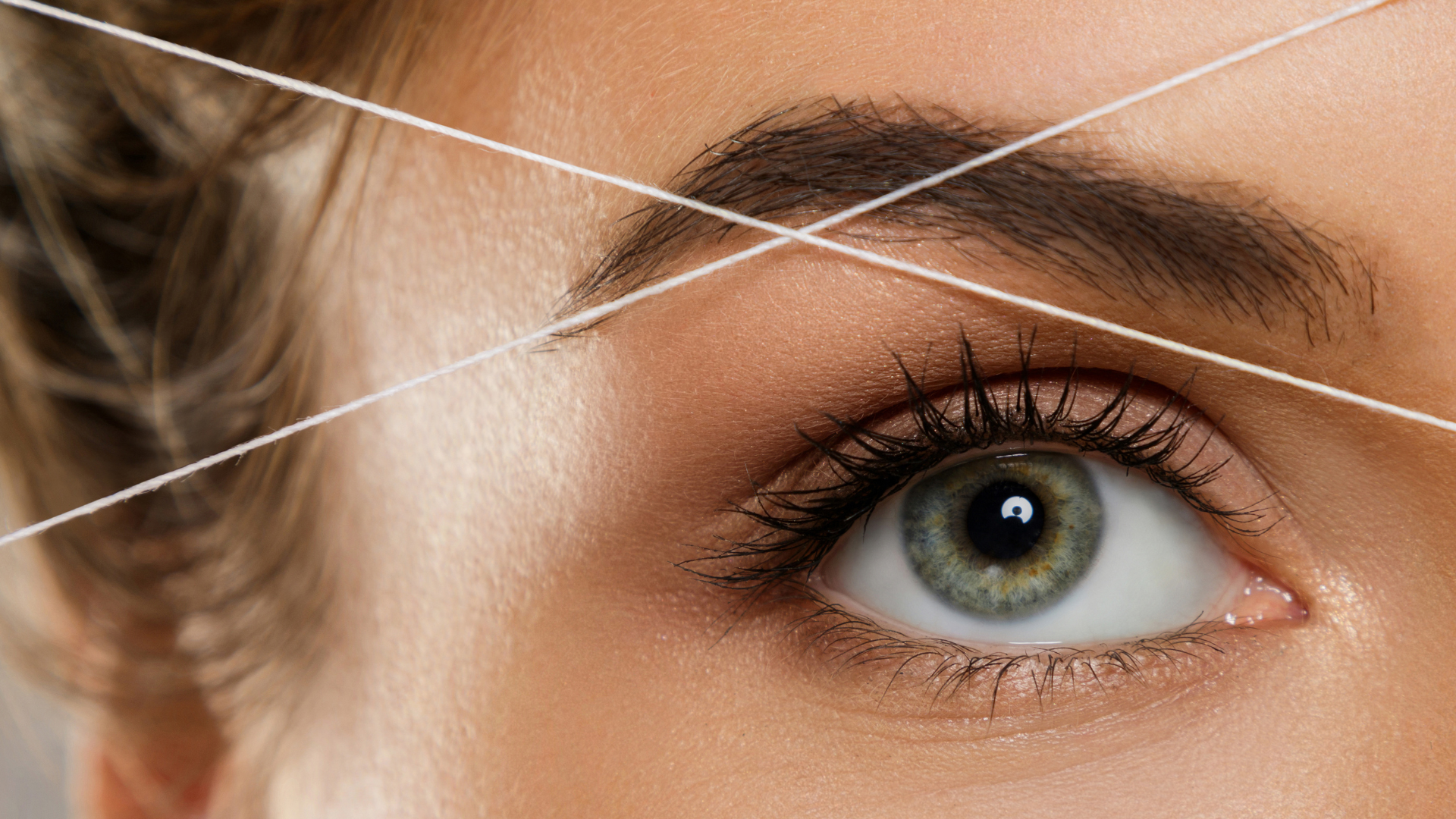 A woman is threading her eyebrows with a string.