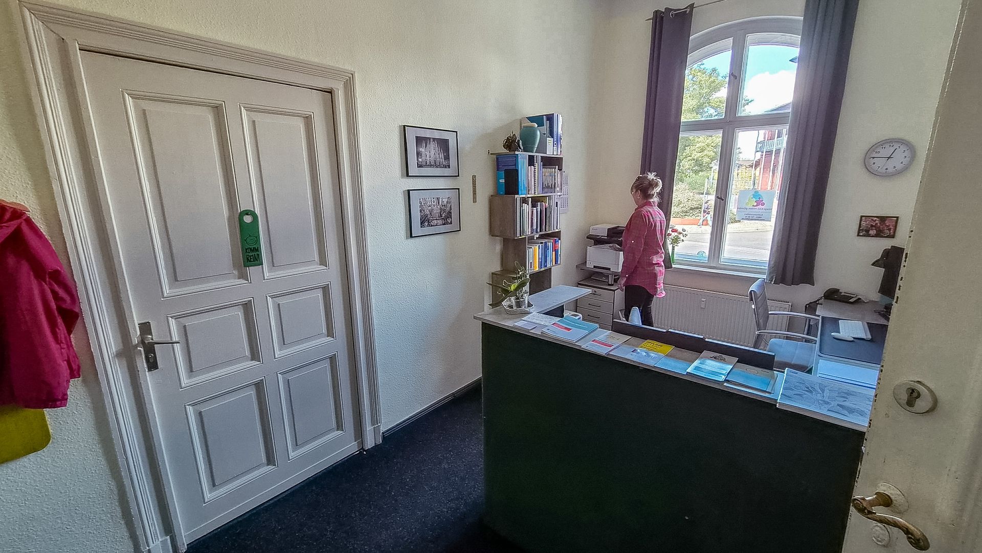 Helle Küche mit einer Person am Spülbecken neben einem sonnenbeschienenen Fenster und einer dunklen Kücheninsel