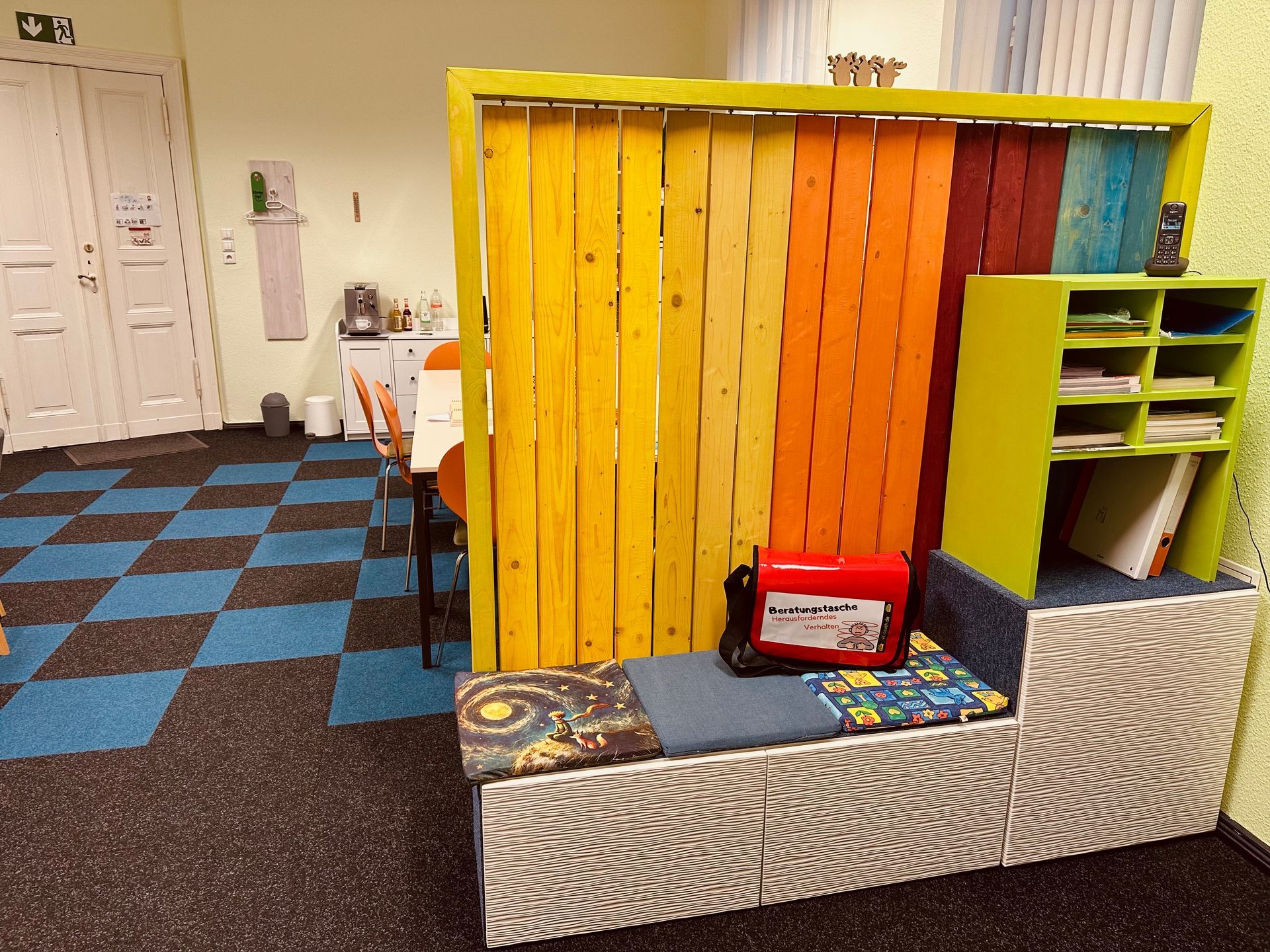 Bunte Holztrennwand in einem Büroraum, mit einer Bank und Fächern.