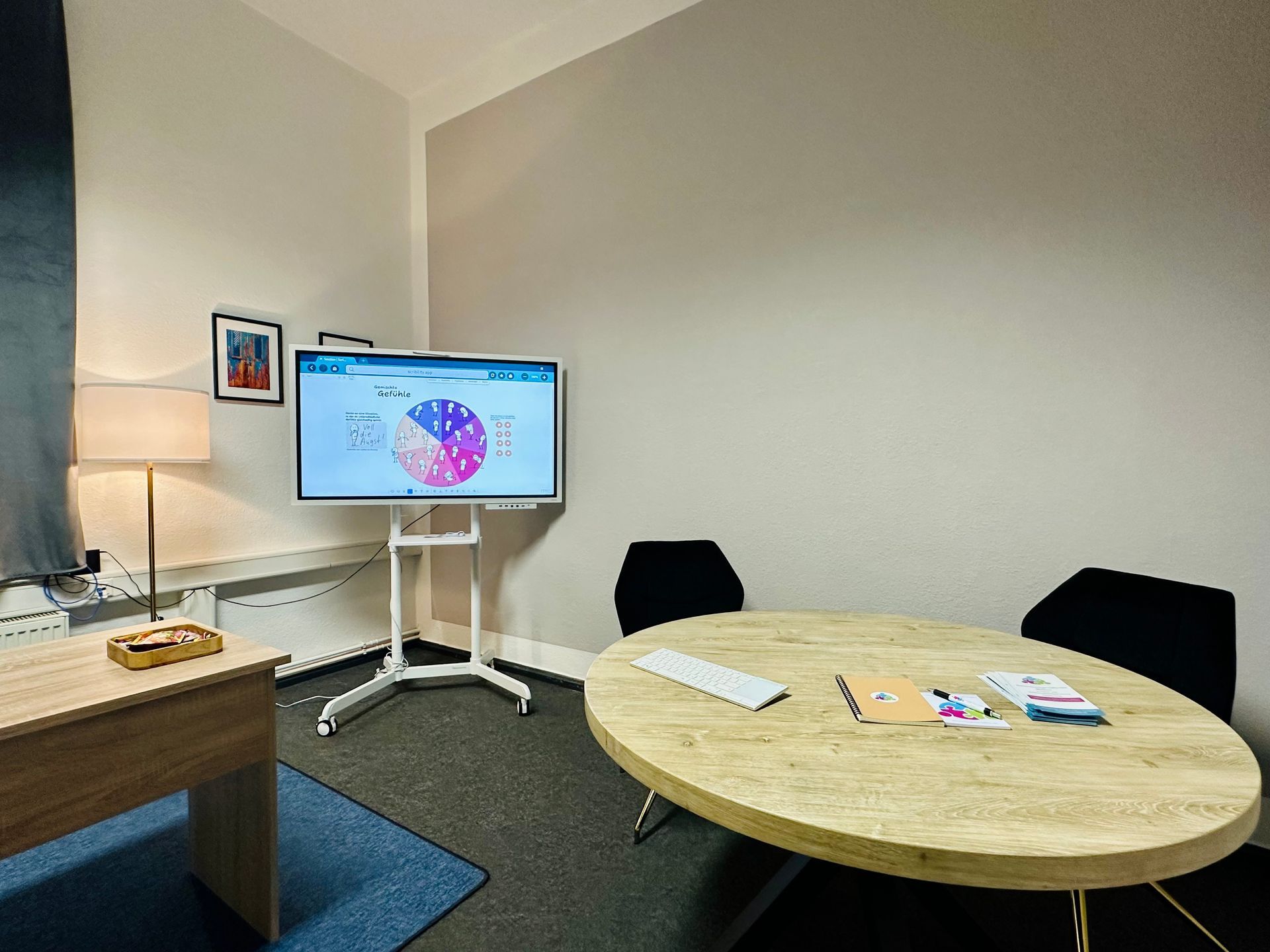 Besprechungsraum mit Monitor, auf dem ein Tortendiagramm angezeigt wird, Tisch, Stühlen und Schreibtisch mit Gegenständen.