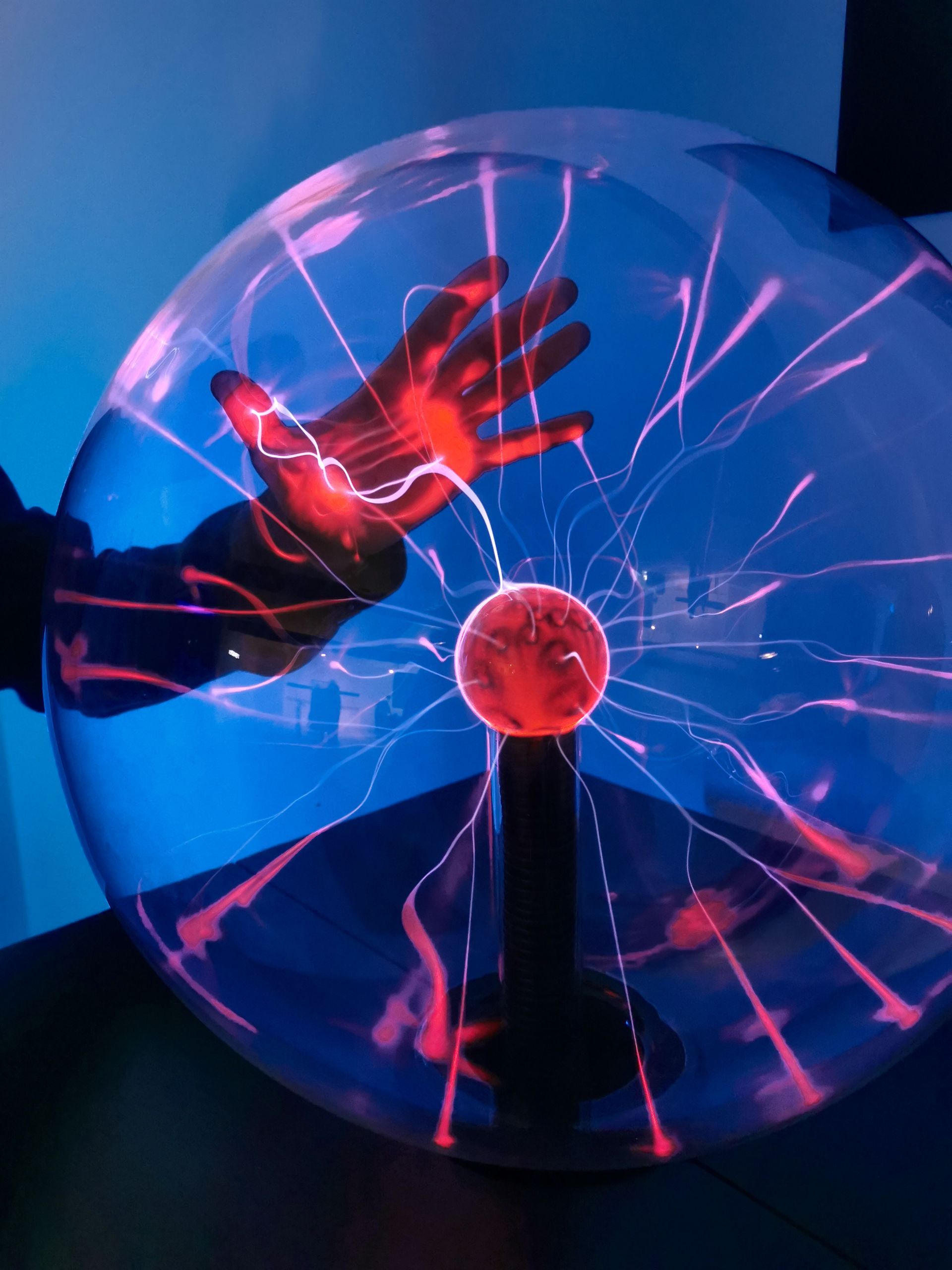 Eine Hand berührt eine leuchtende Plasmakugel mit pinkfarbenen elektrischen Bögen vor dunkelblauem Hintergrund