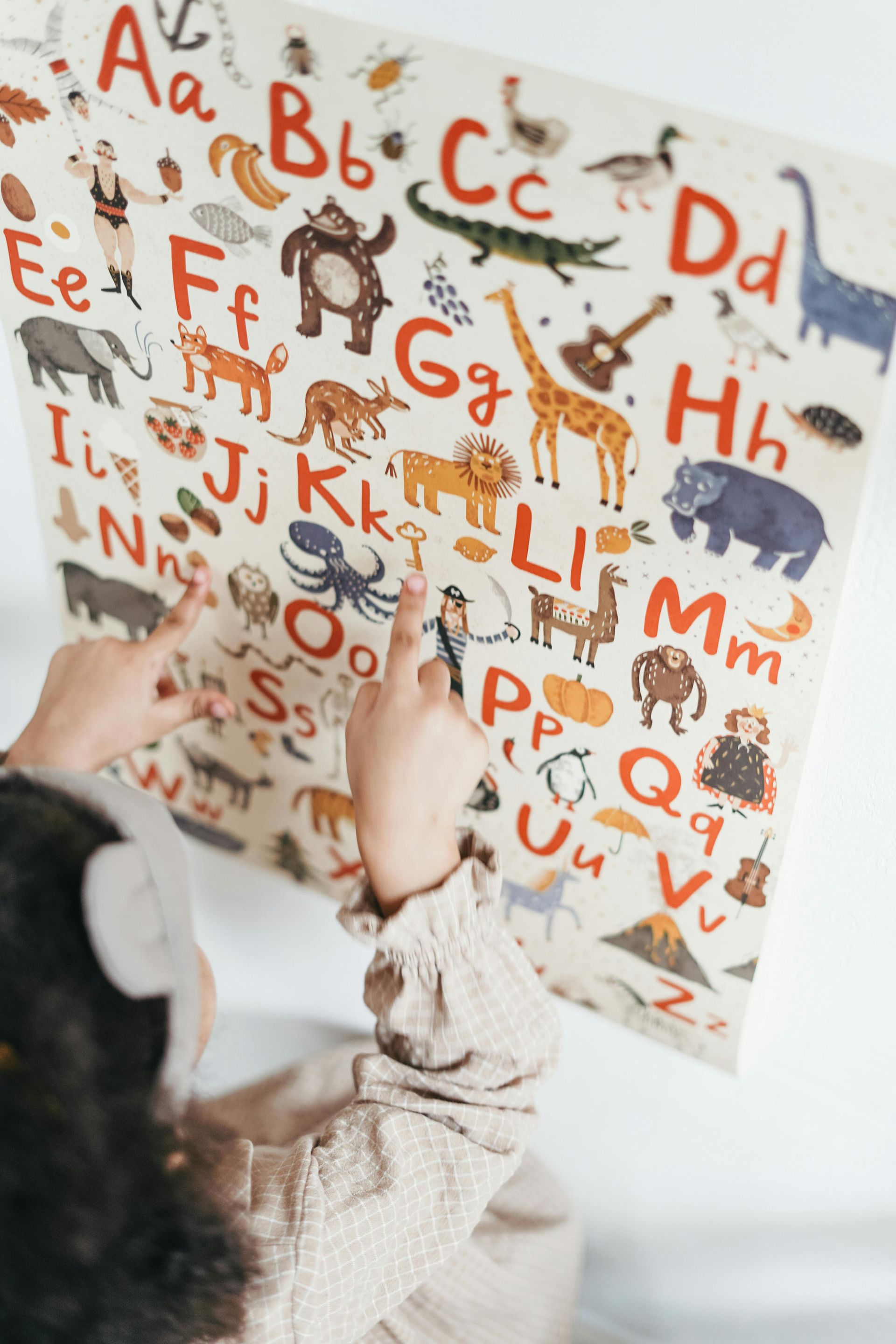 Kind zeigt auf eine Alphabettafel mit Illustrationen.