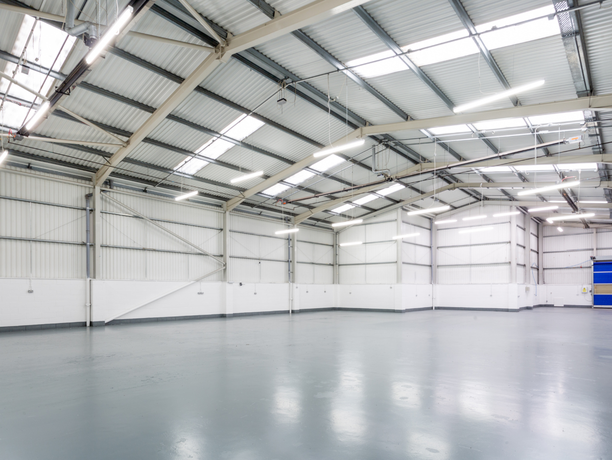 Empty warehouse interior with grey floor and white walls, skylights in the metal roof.