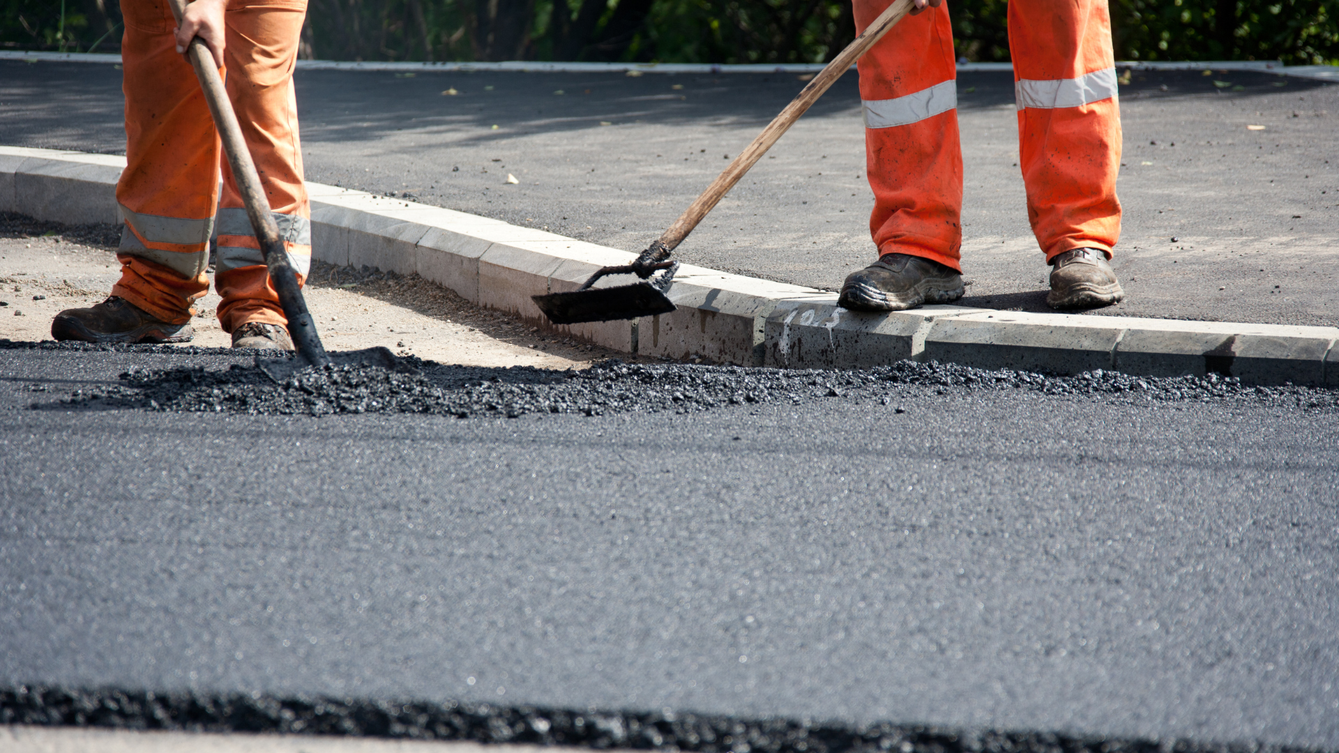 Road workers in orange vests smoothing fresh asphalt with a broom on a street repair site