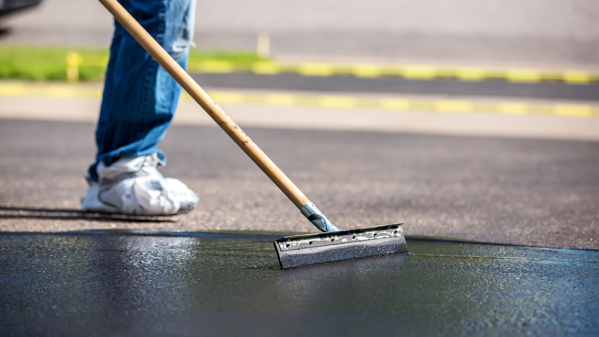 Person using a roller to paint dark asphalt on a road surface