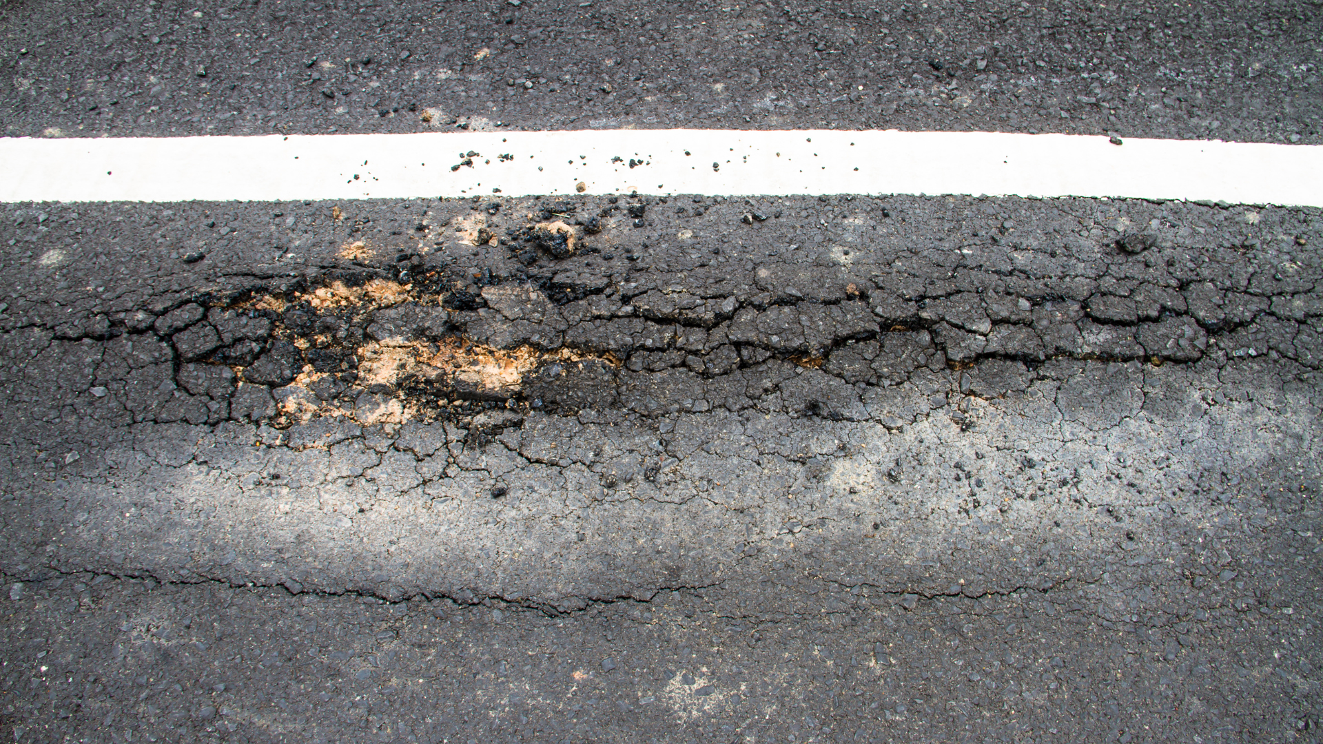 Road roller compacting a dark asphalt patch on a concrete surface
