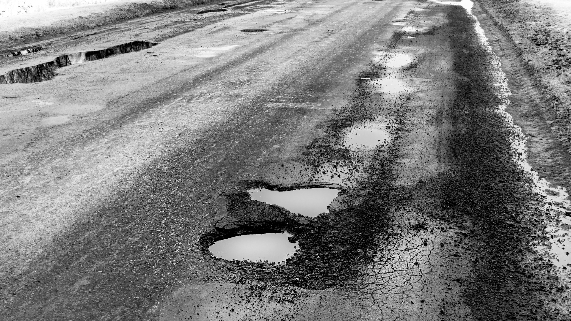 Potholes and cracks in a rough, snow-dusted road surface
