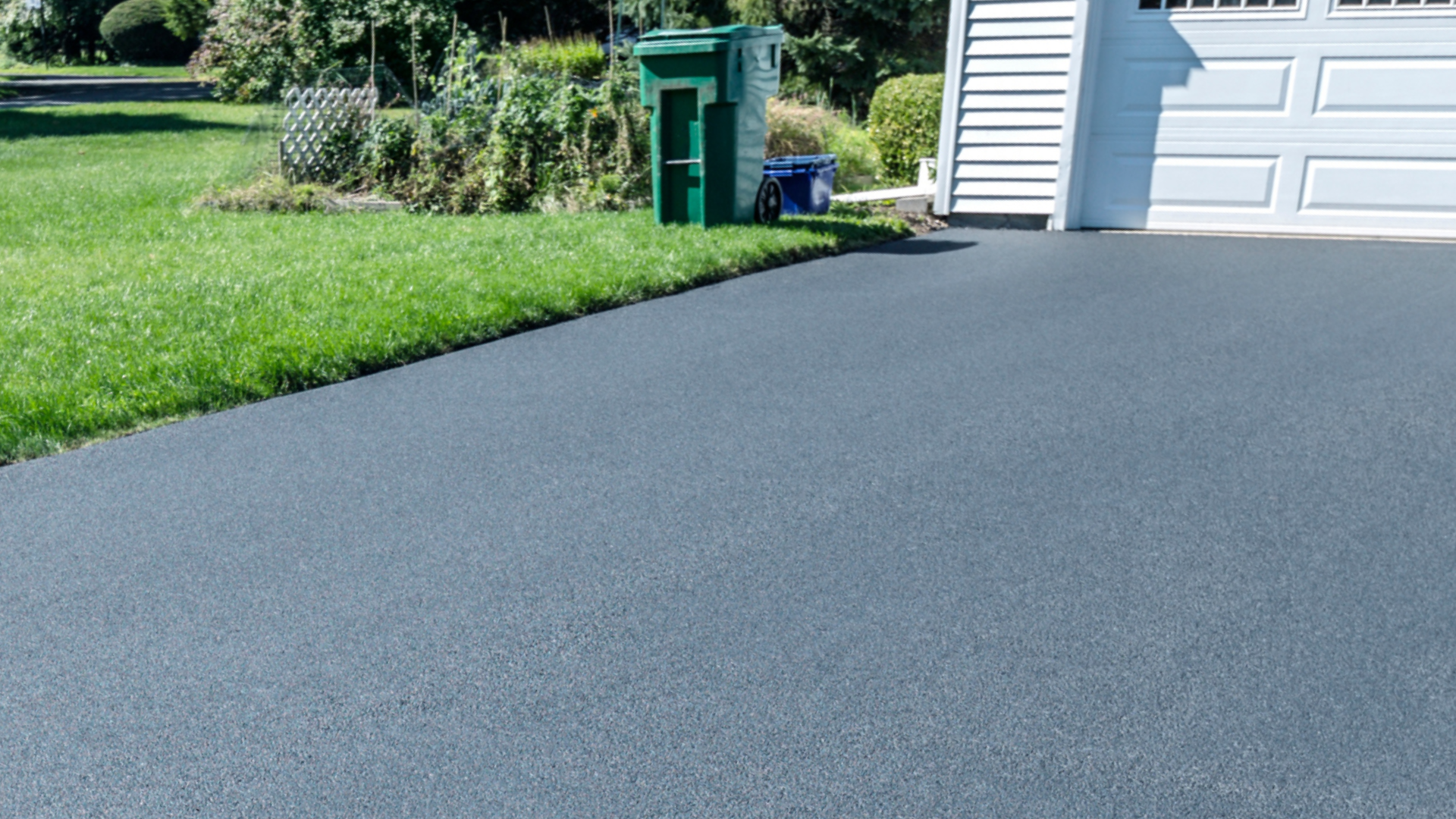 Freshly paved driveway beside a white garage and green lawn, viewed at a slight angle