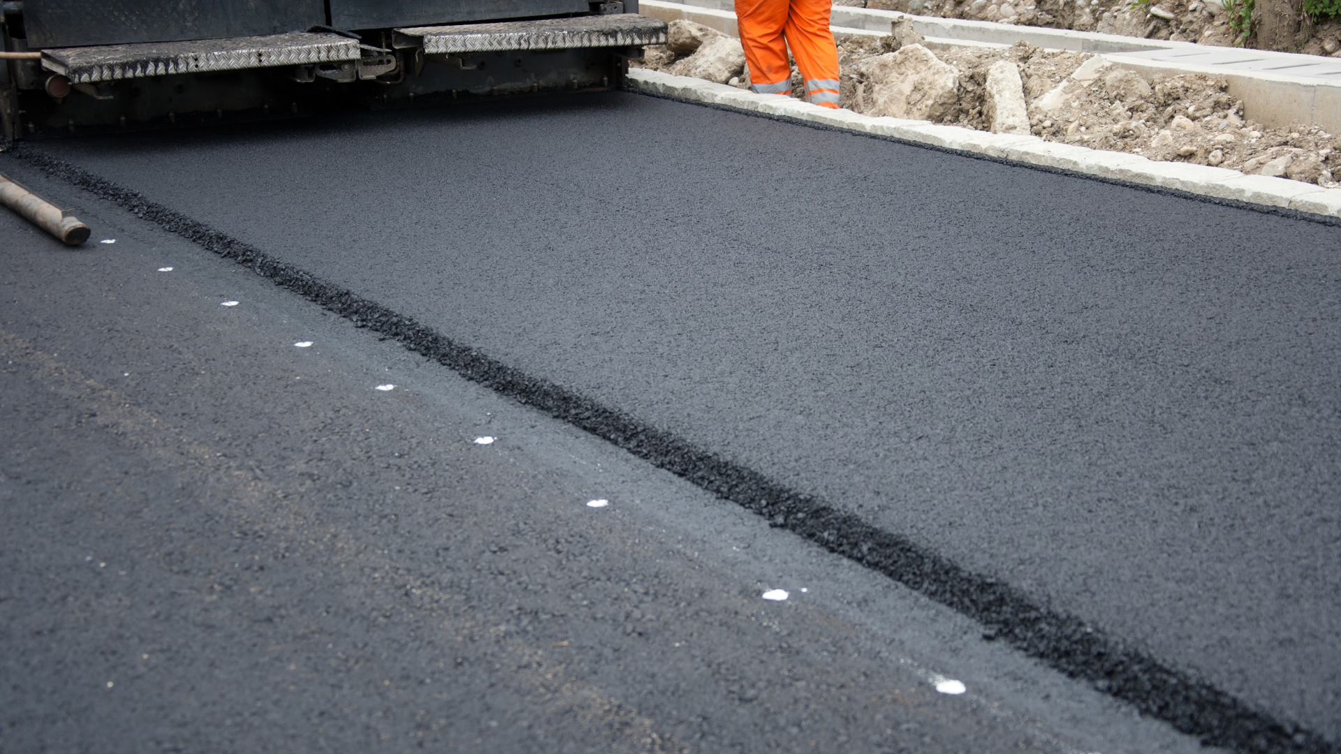 Road paving machine laying fresh black asphalt on a street, with workers visible in the background