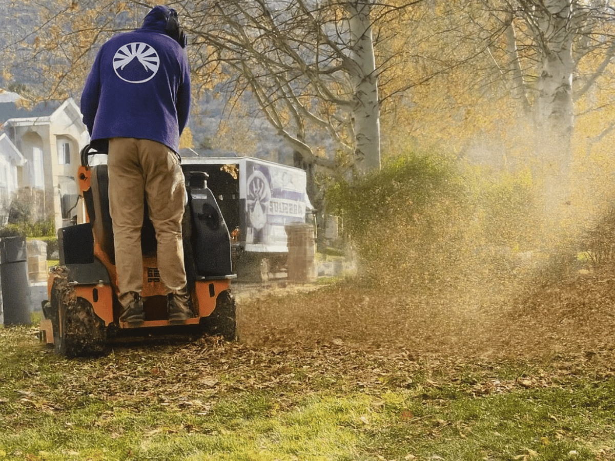 SolTerra technician on a small orange machine blowing leaves on a lawn; a white truck in the background.