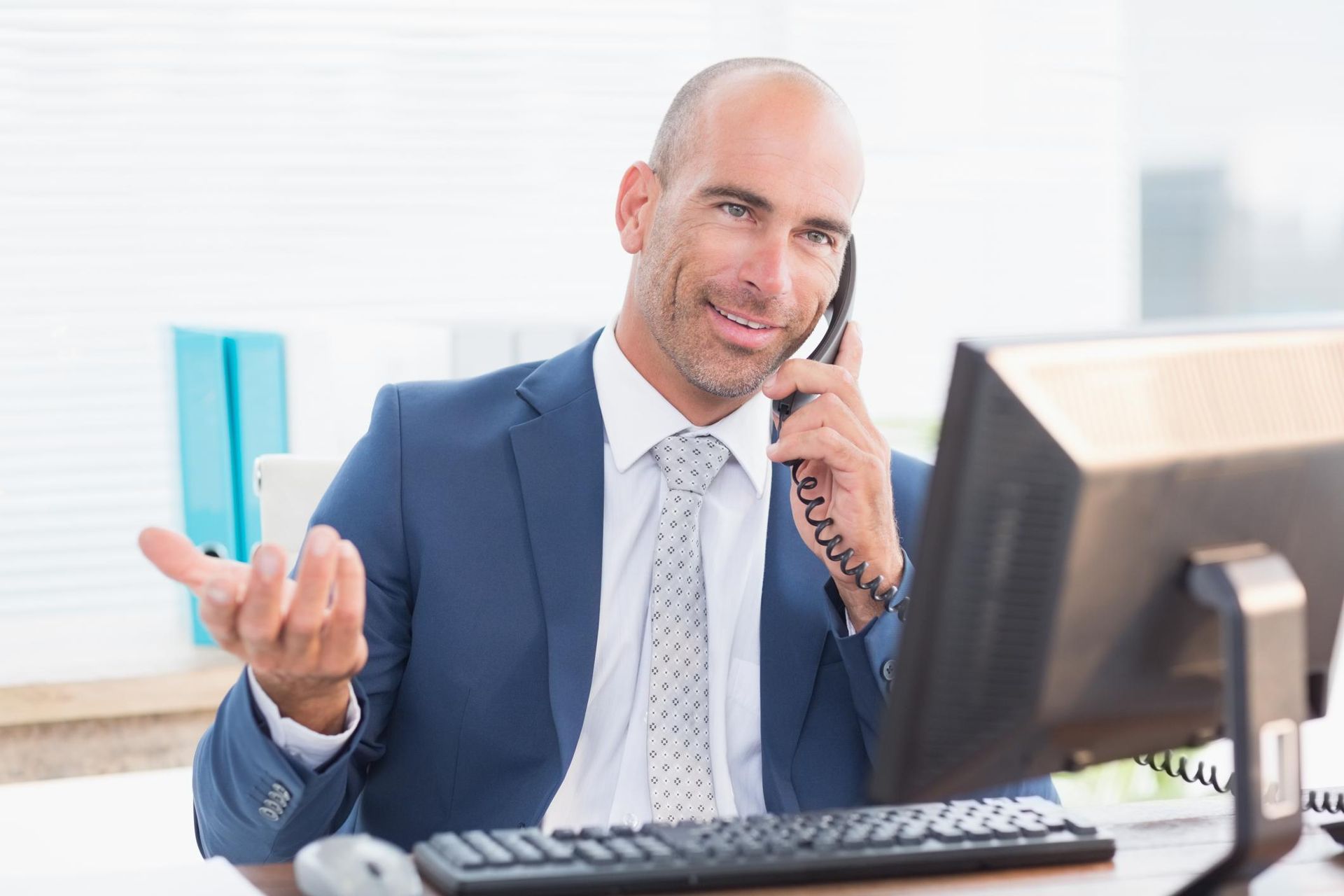 A man in a suit and tie is talking on a phone in front of a computer