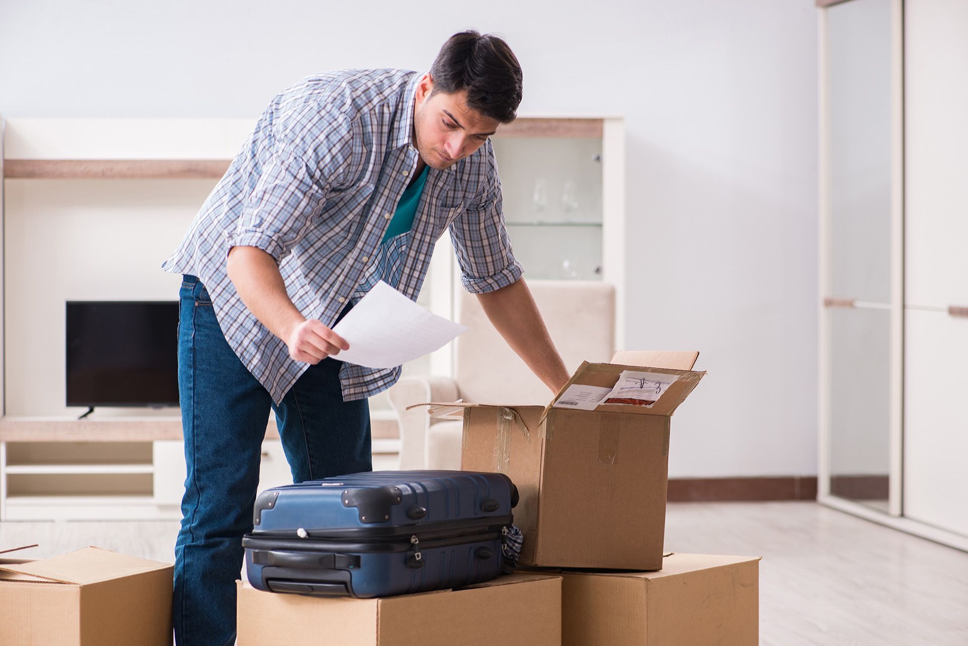 A man is standing next to a suitcase and boxes in a living room.