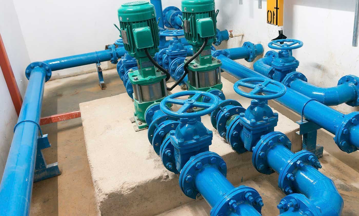 Tuberías de agua azules y dos bombas verdes en un entorno industrial.