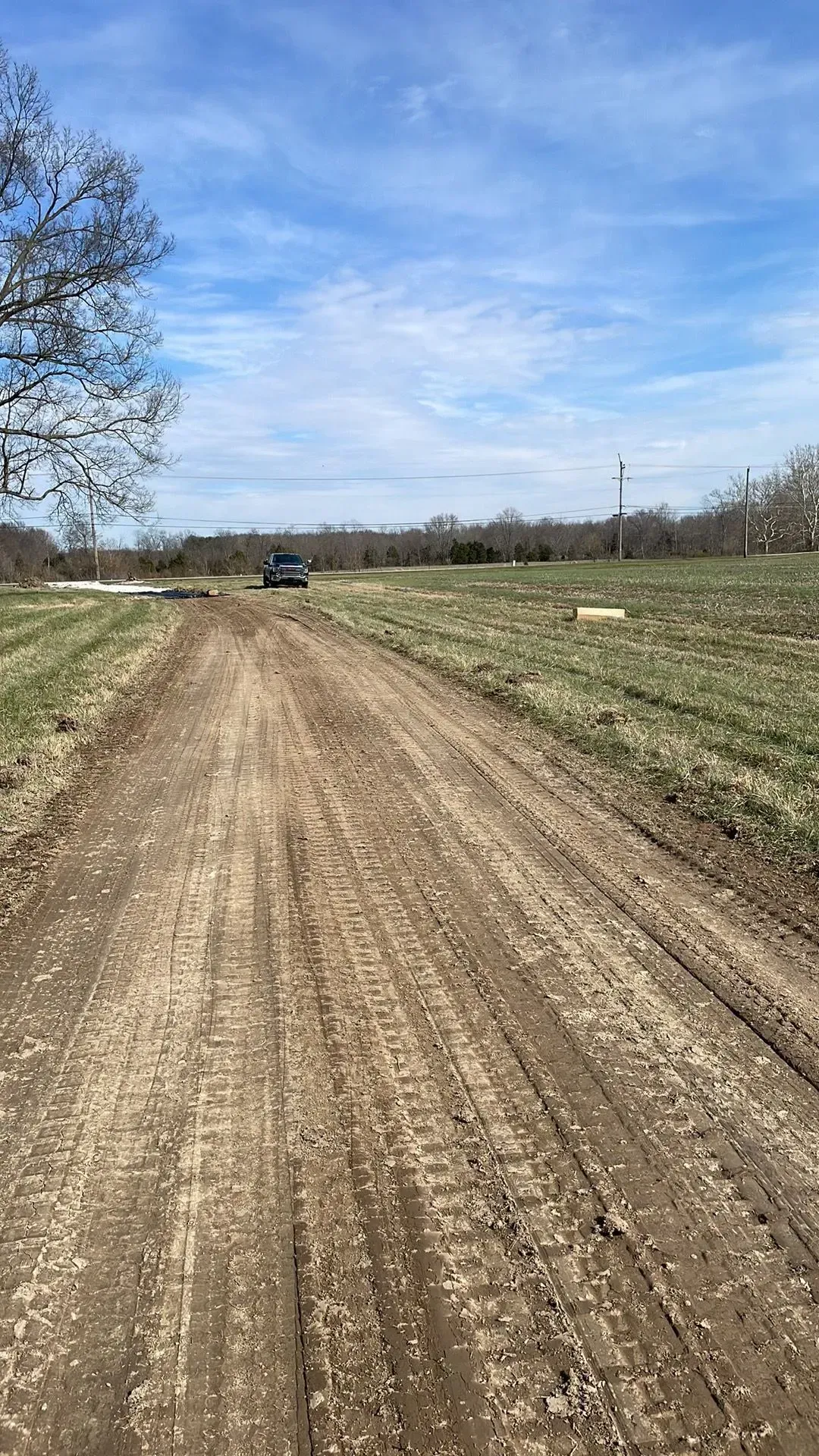 Dirt road through open fields under a blue sky, with a small car in the distance.