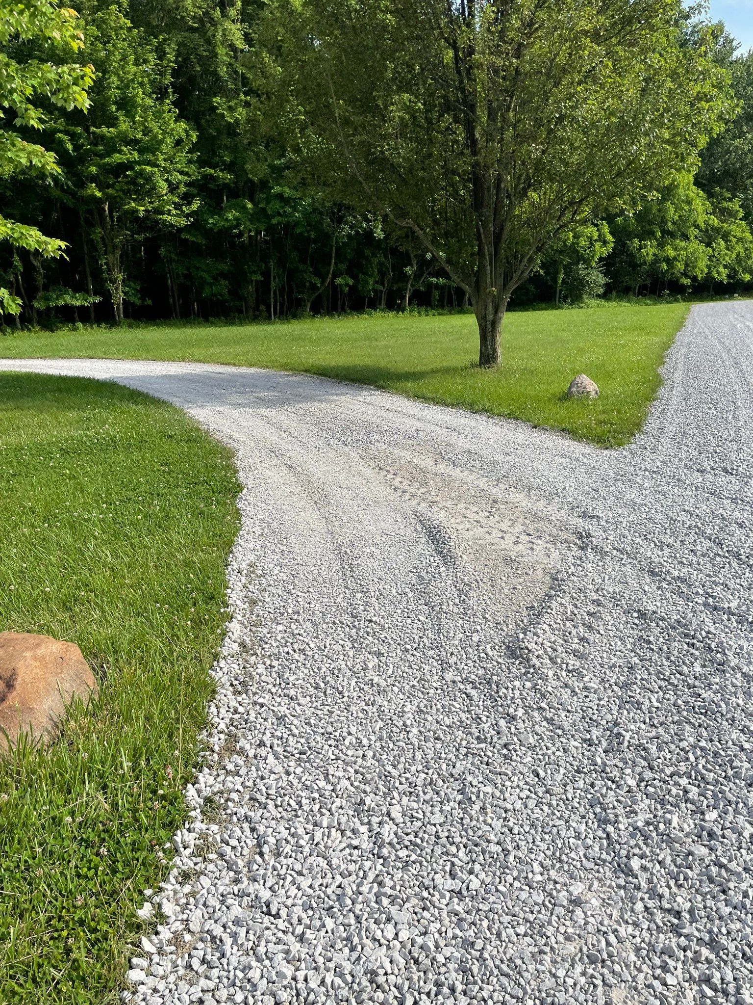Gravel driveway curves through a green yard with trees on both sides