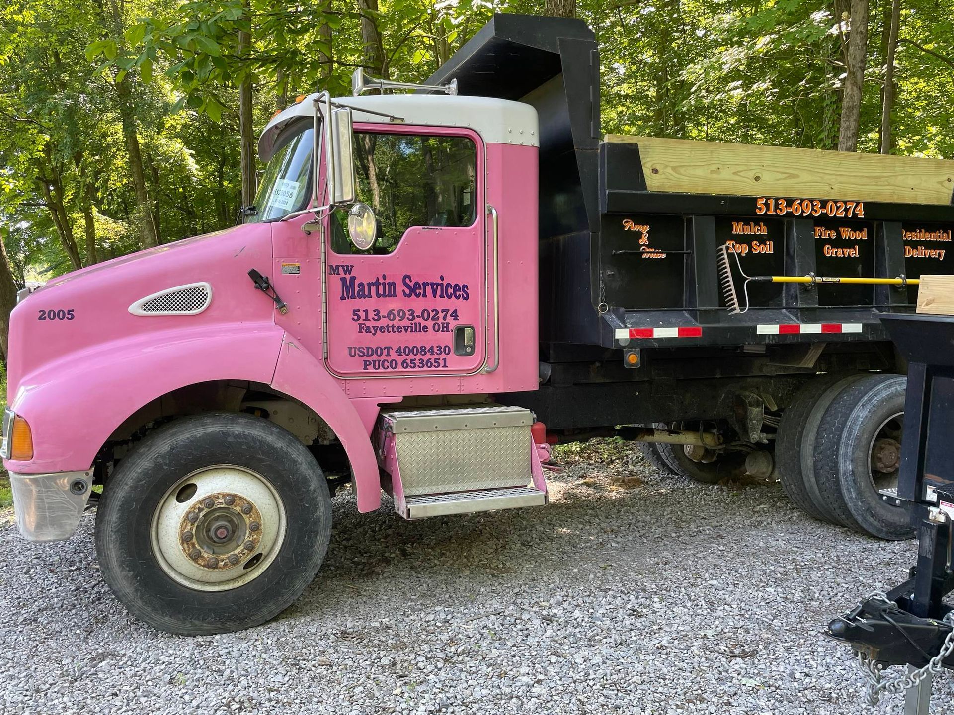 Pink Martin Services dump truck parked on gravel beside trees