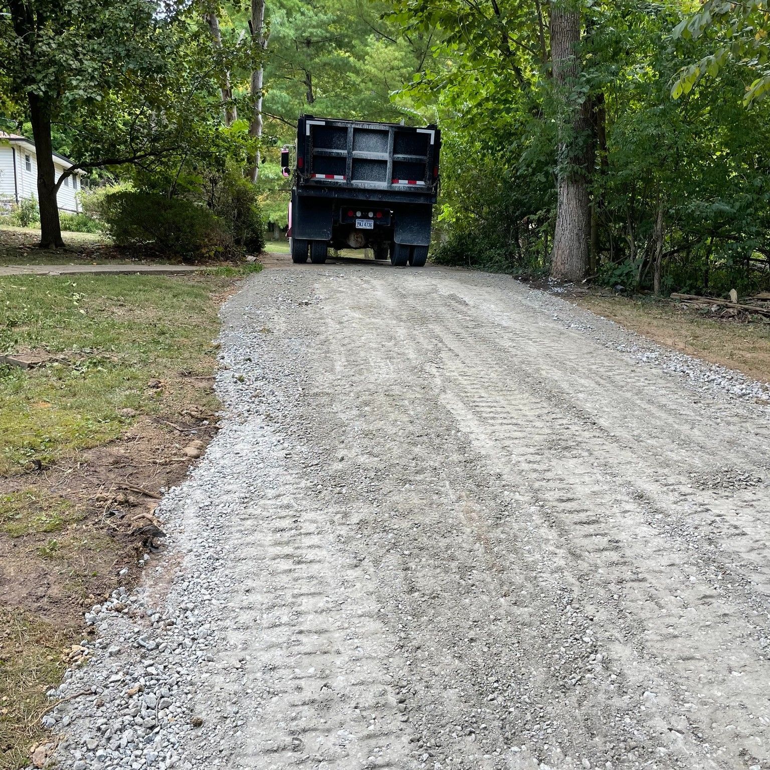Gravel driveway in a wooded area with a black dump truck parked at the top