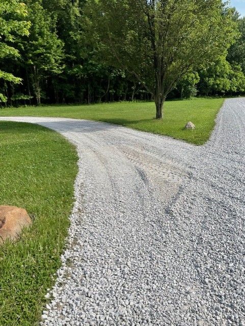 Curving gravel driveway through green grass and trees on a sunny day