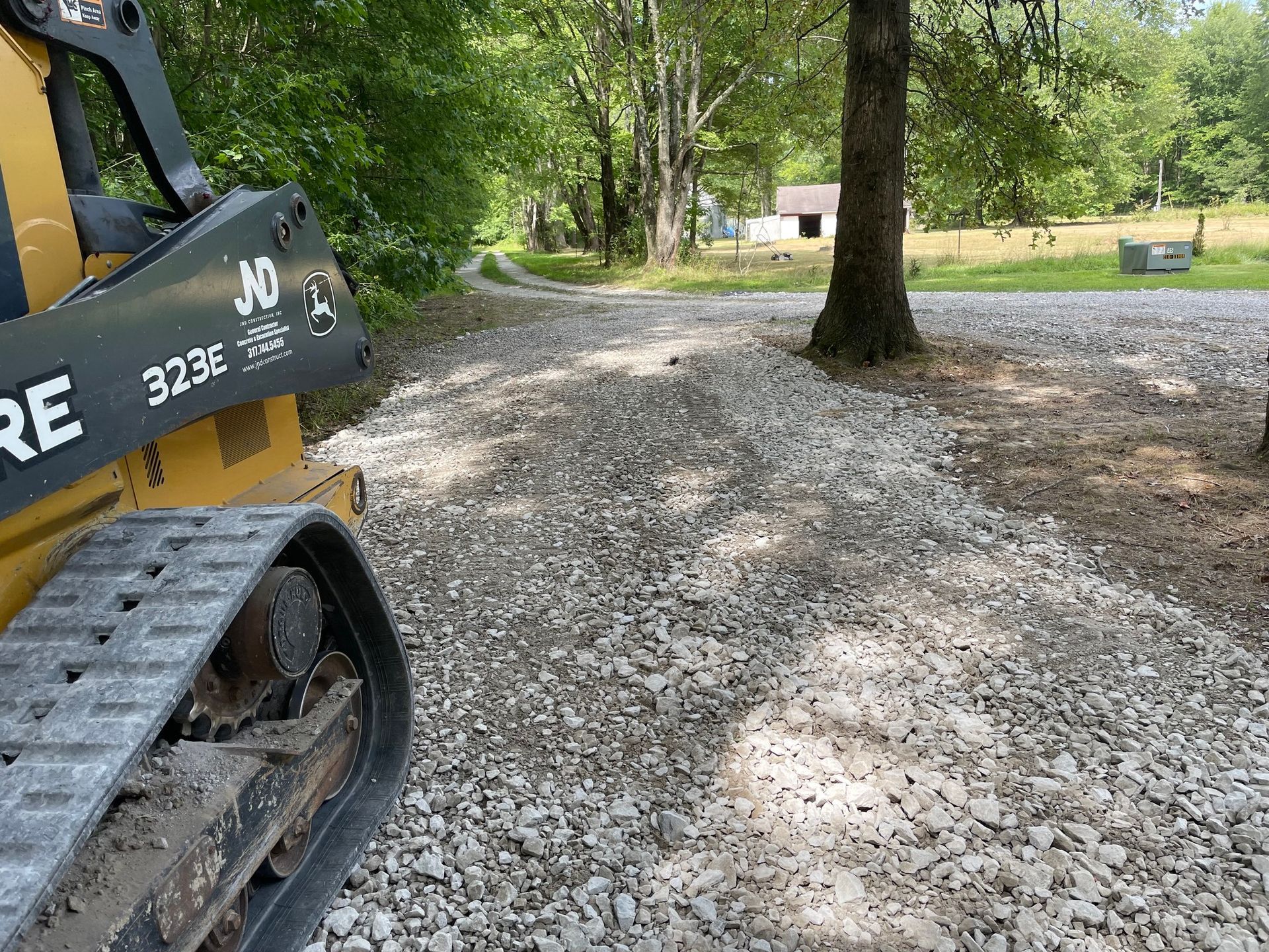 Yellow excavator on gravel driveway beside a tree in a wooded yard