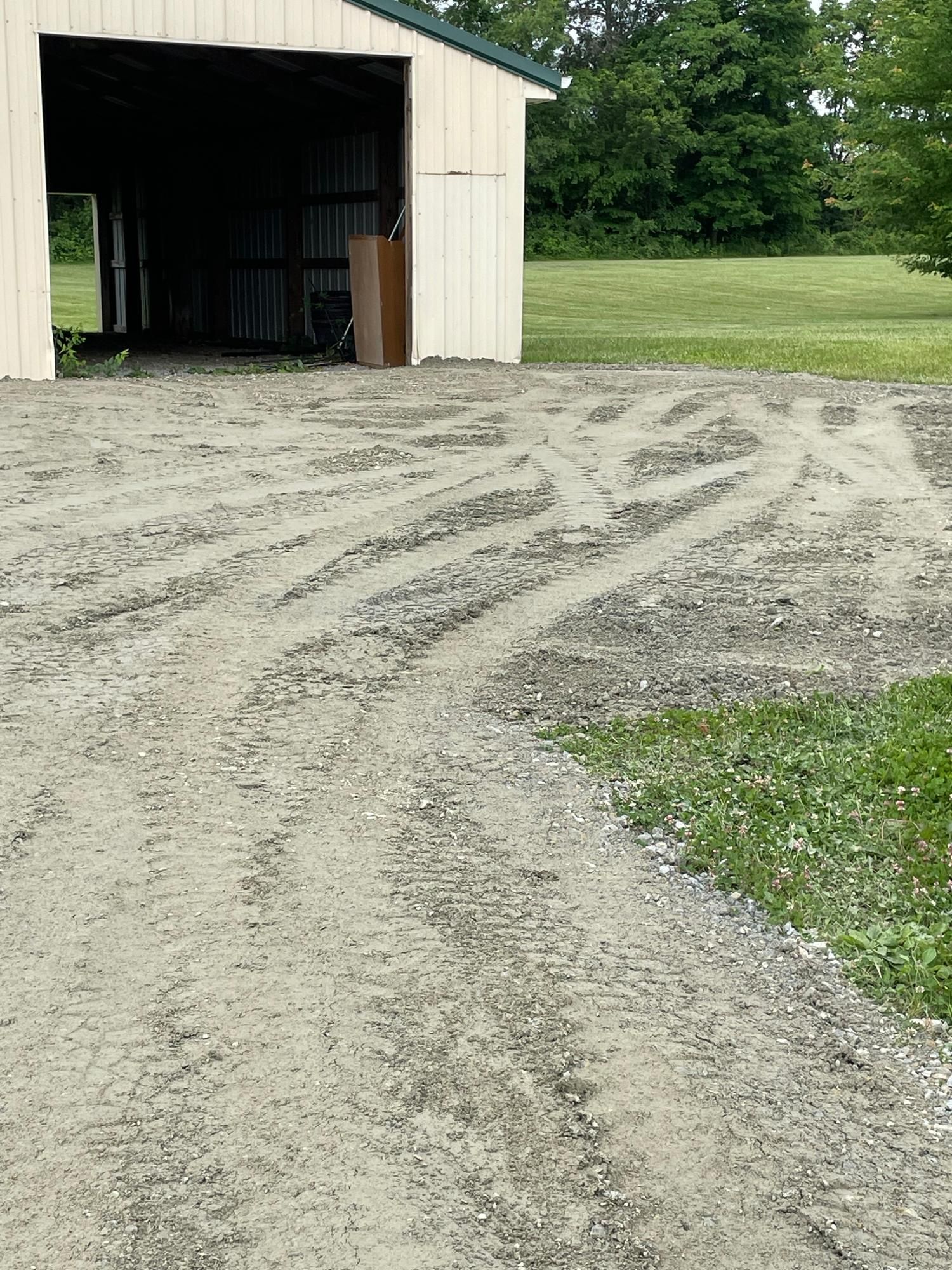 Gravel driveway leading to an open beige shed in a grassy rural area