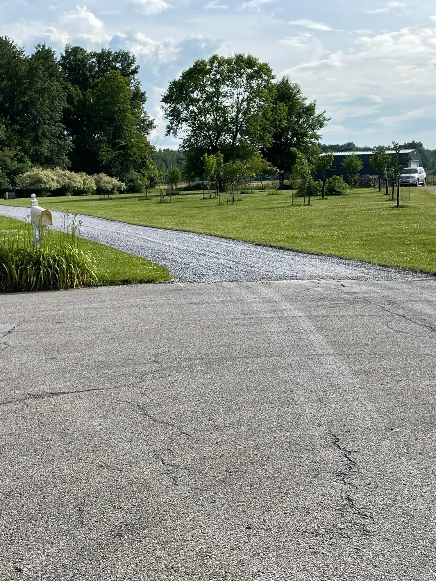 Gravel path winding through a green park with trees and a paved foreground