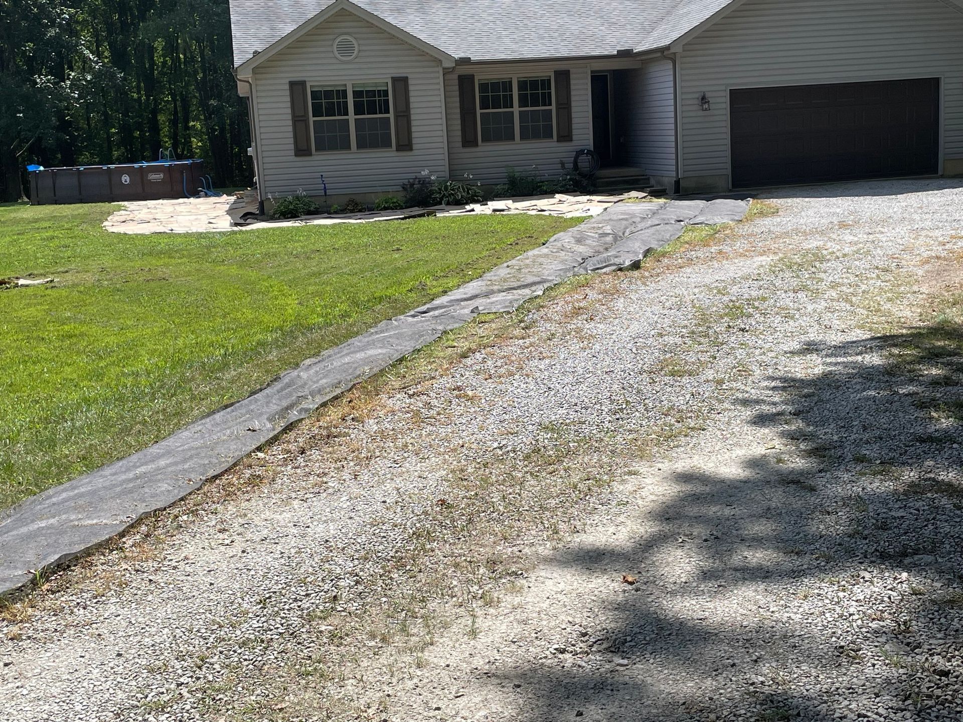 Single-story house with a gravel driveway, green lawn, and attached garage in bright daylight