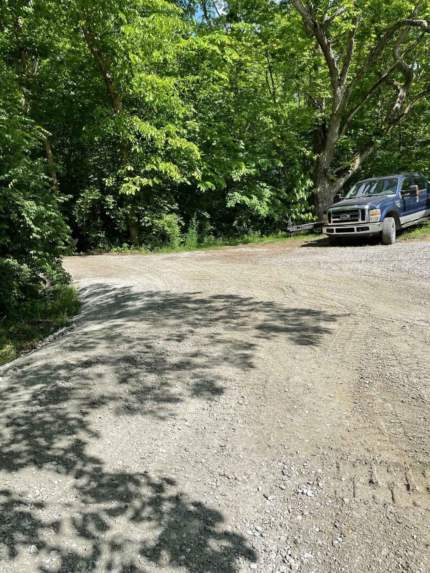 Gravel road winding through a leafy forest, with a parked SUV on the right.
