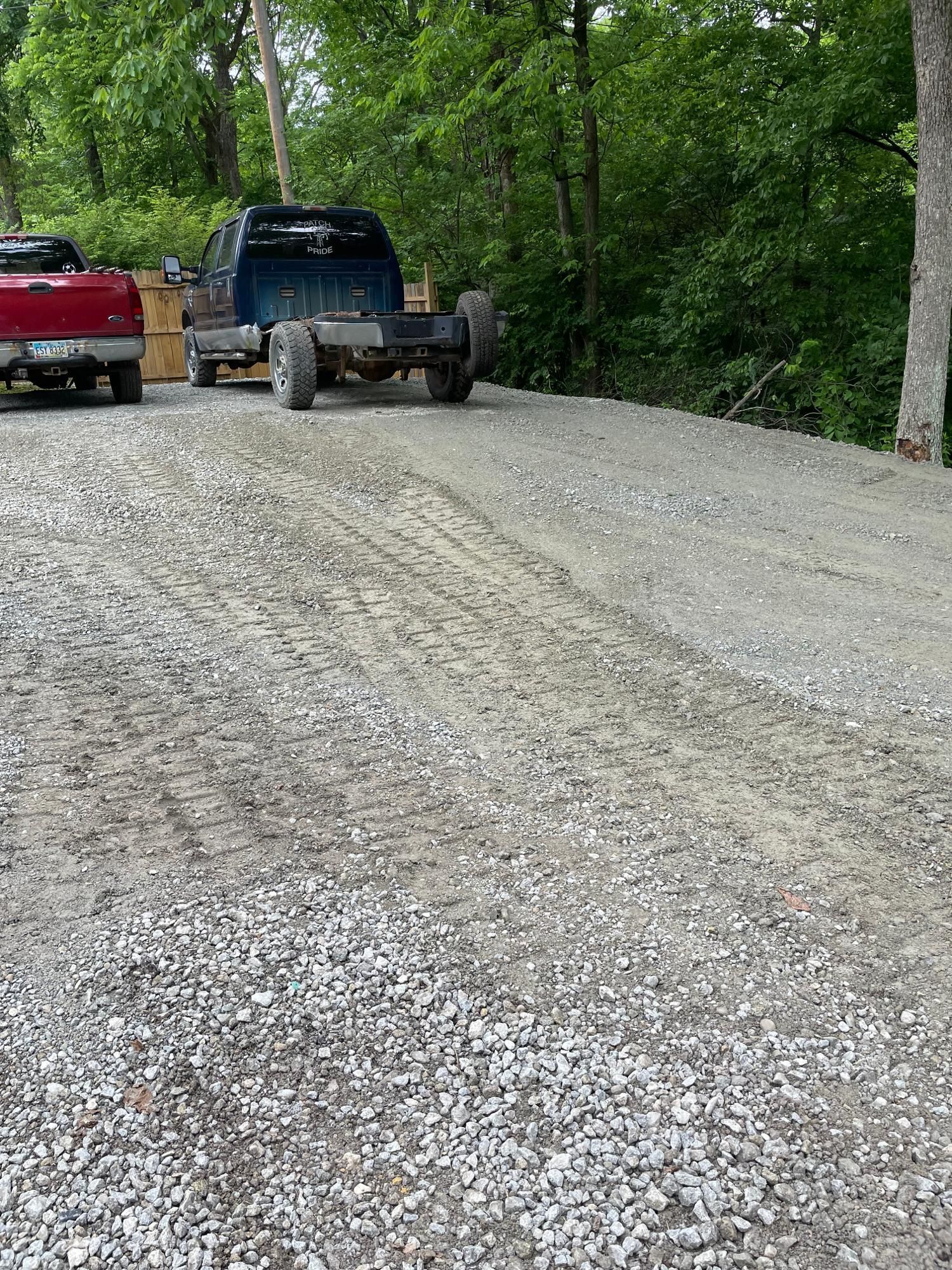 Gravel road with two parked trucks beside green trees on a curving hillside