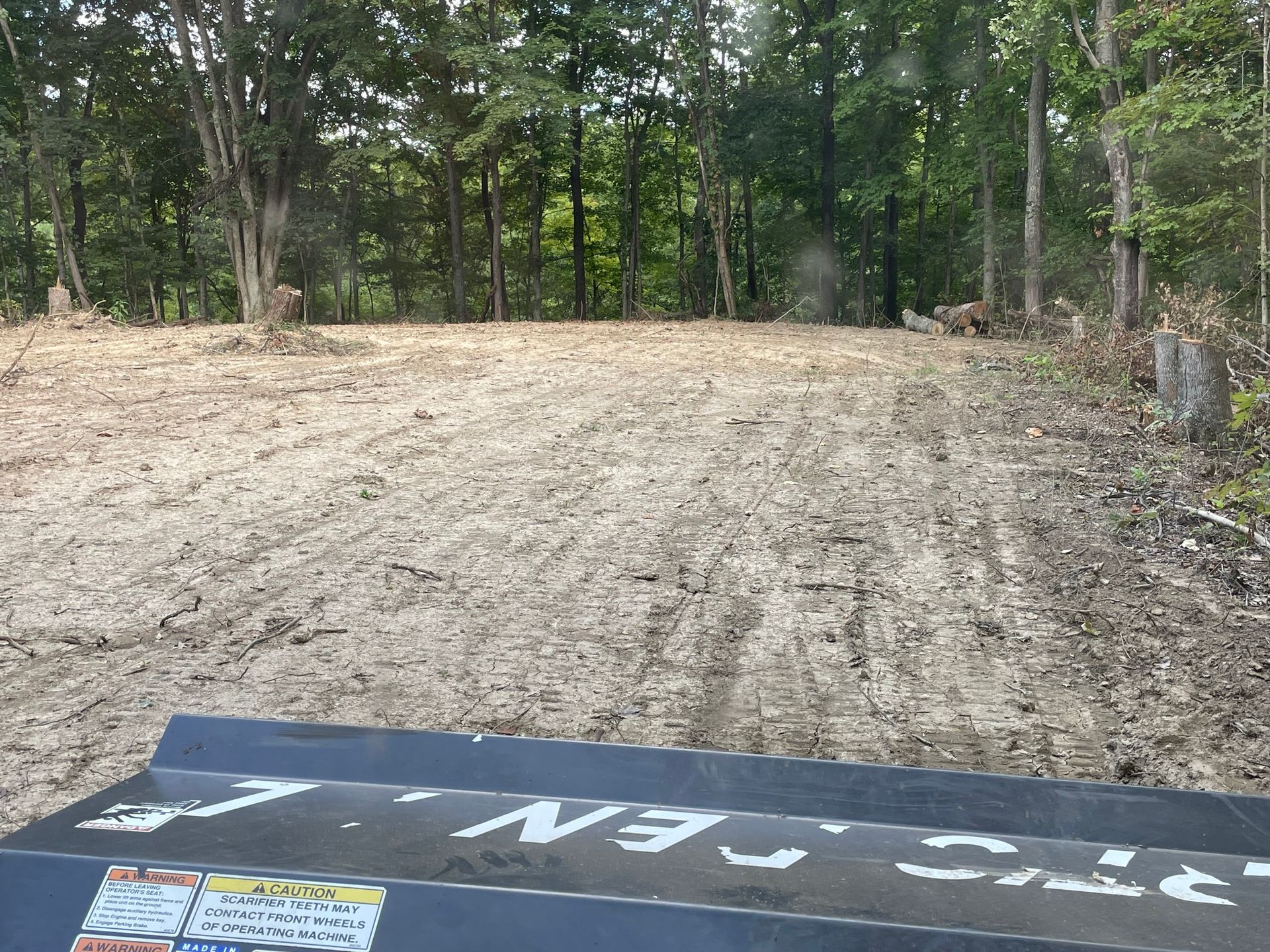 Empty dirt clearing bordered by trees, with a blue sign partially visible in the foreground.